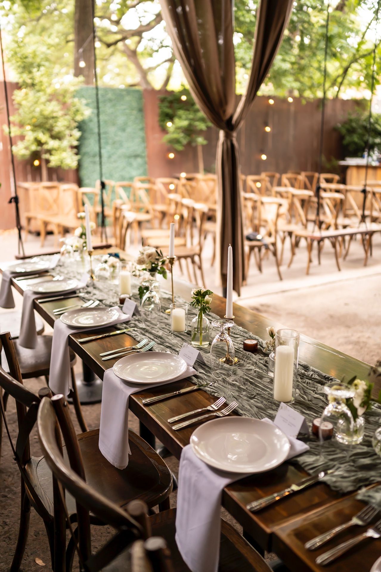 Elegant outdoor wedding reception table setup with rustic wooden tables, white napkins and romantic string lights overhead.