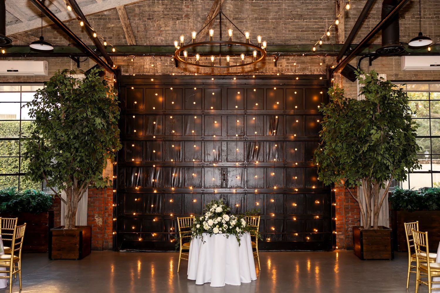 Rustic indoor wedding venue with exposed brick walls, string lights, and elegant table settings creates a warm ambiance.
