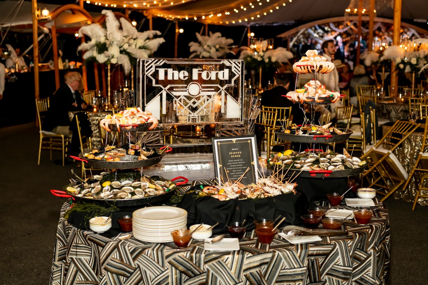 Wedding reception dessert and food station with geometric patterned tablecloth under string lights at night.