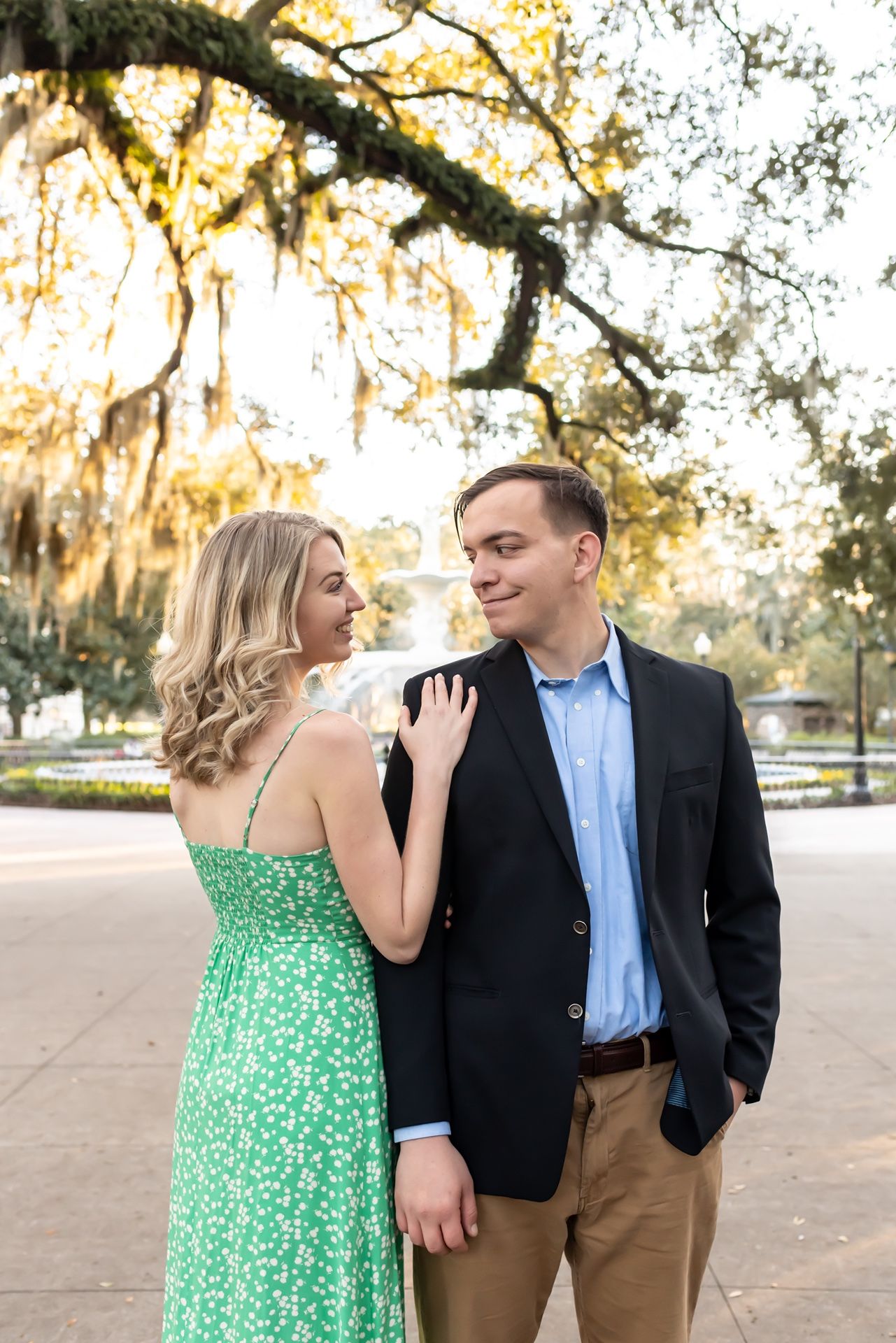 A couple shares a romantic moment beneath Spanish moss draped trees during golden hour in a park setting.