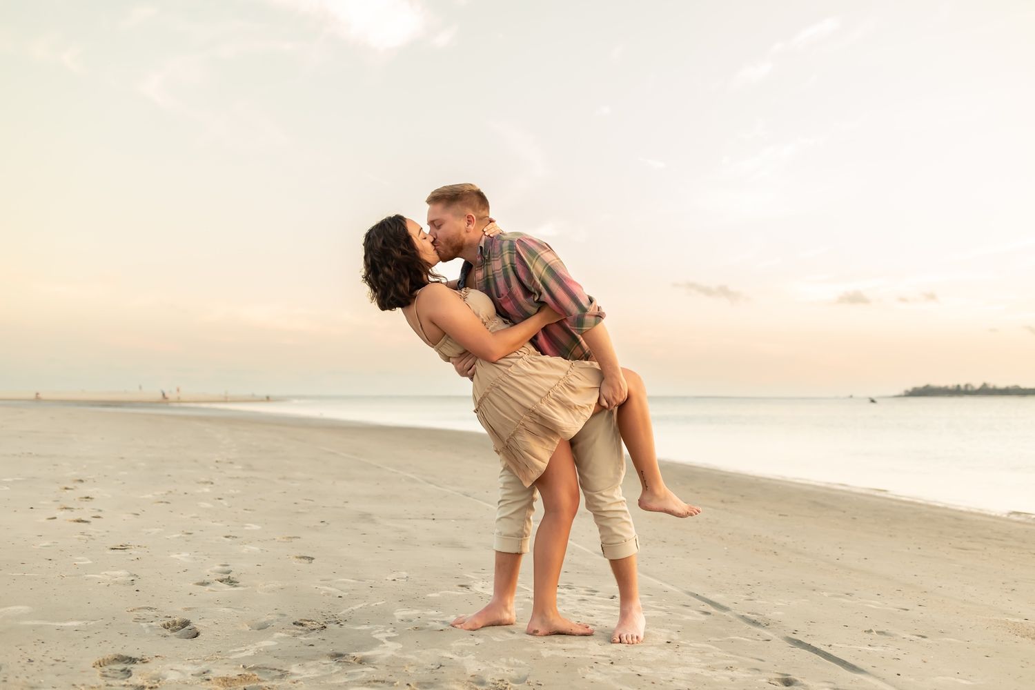 A romantic couple walks hand in hand along a serene beach at sunset during their barefoot coastal stroll.