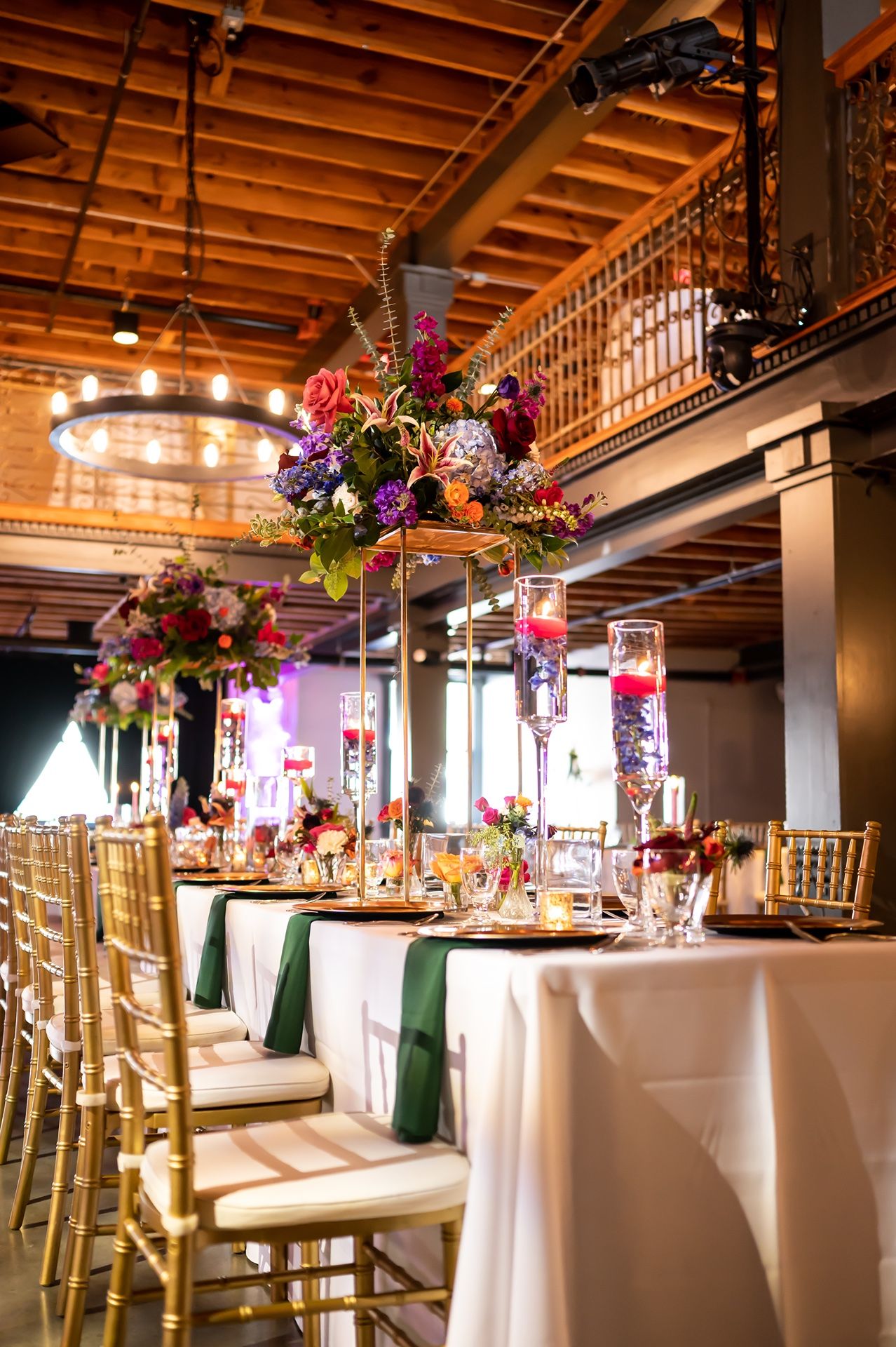 Elegant wedding reception venue with tall floral centerpieces, gold chiavari chairs and white tablecloths with green accents.