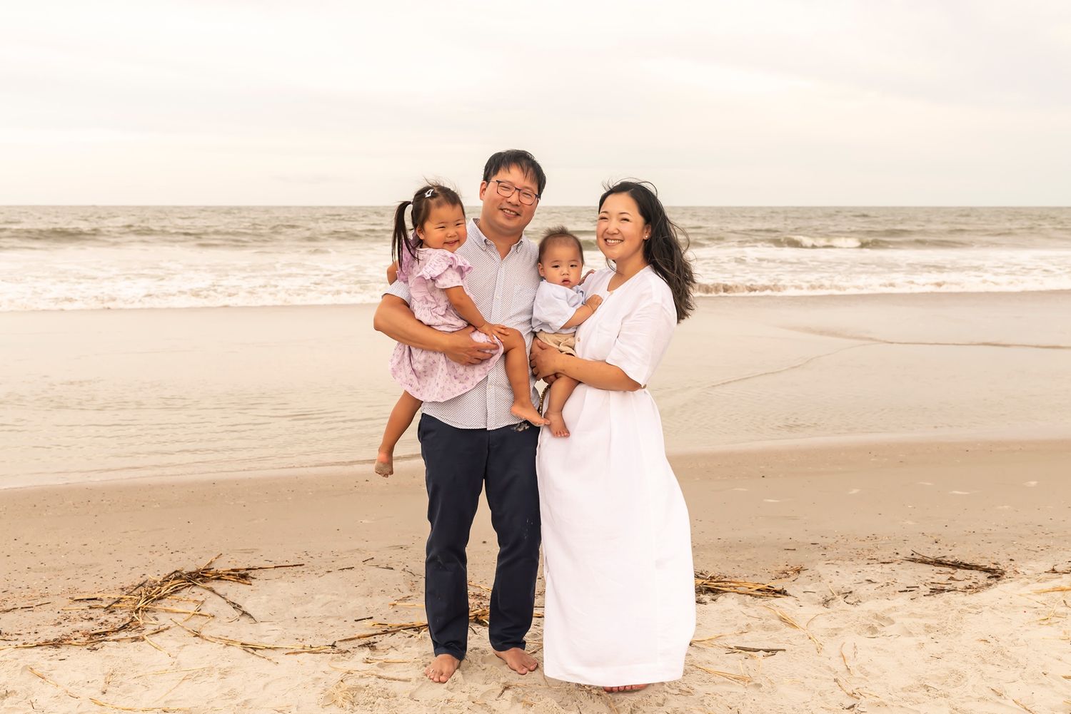 A loving family walks together on a sandy beach wearing white and navy outfits while sharing joyful moments.