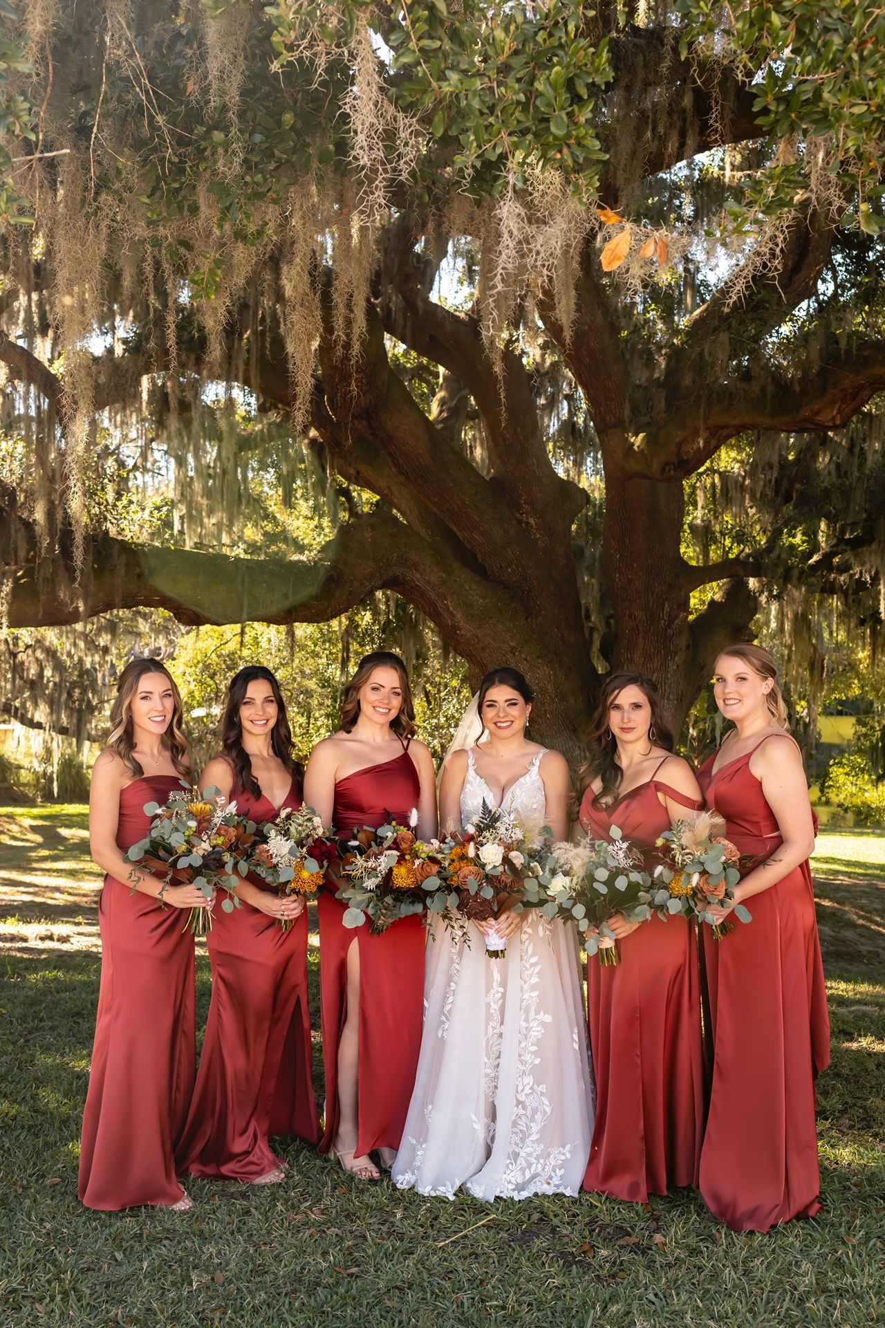 A wedding party poses under a majestic oak tree draped with Spanish moss in a Southern garden setting.