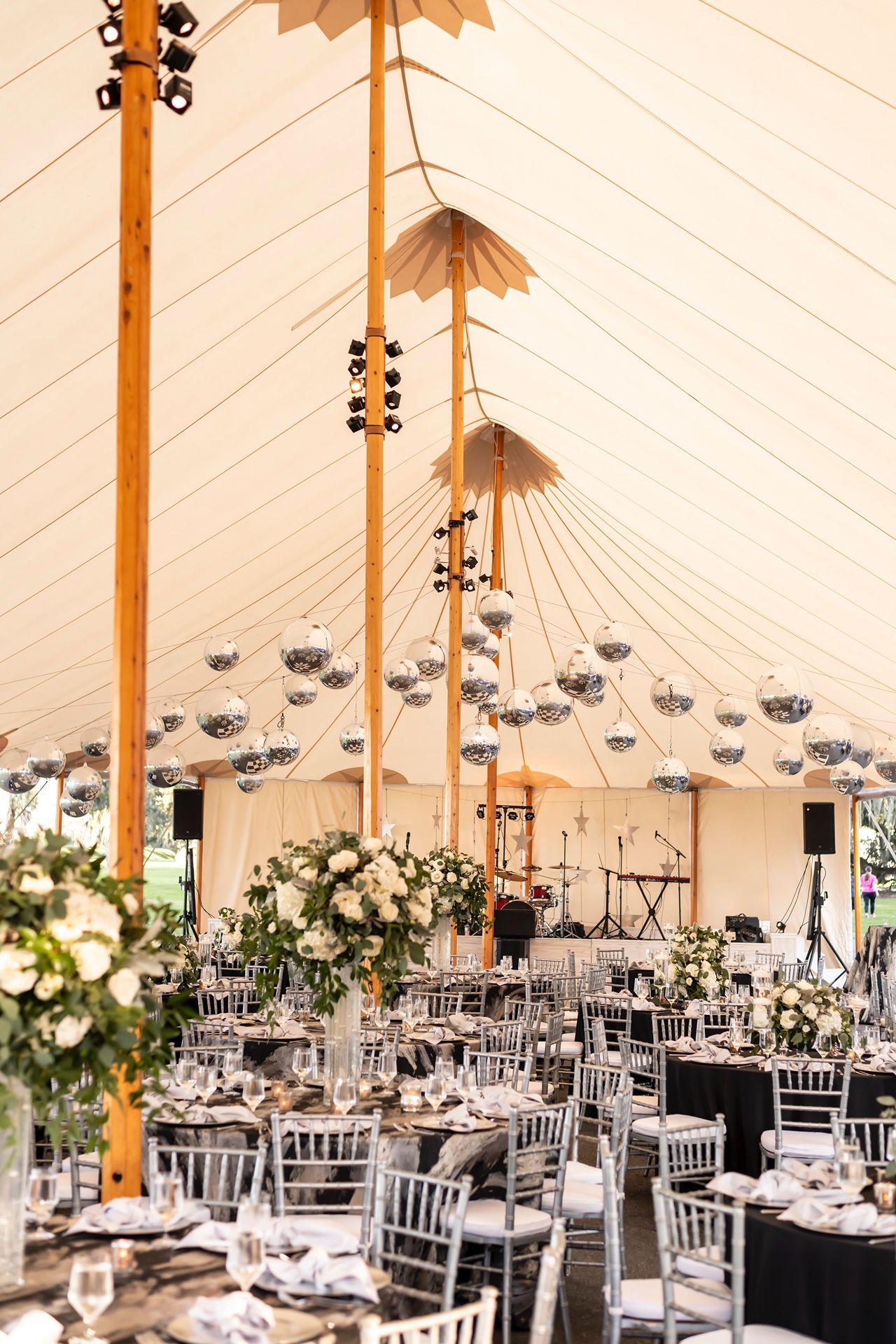 Elegant wedding reception setup in a white tent with crystal chandeliers, Chiavari chairs and formal table settings.