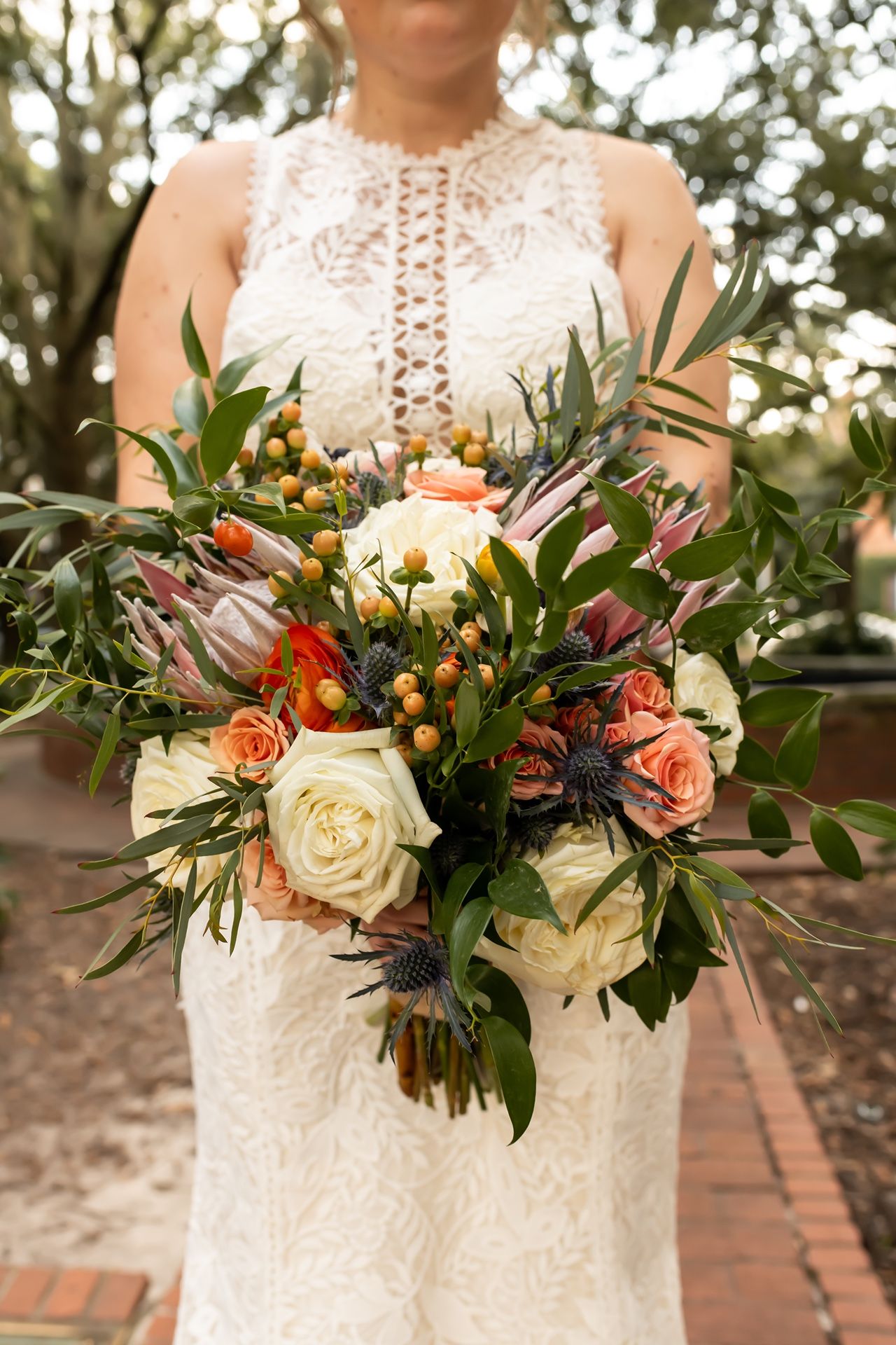 A wedding bouquet features white roses, orange blooms, dark burgundy flowers and lush greenery in an autumn-inspired arrangement.