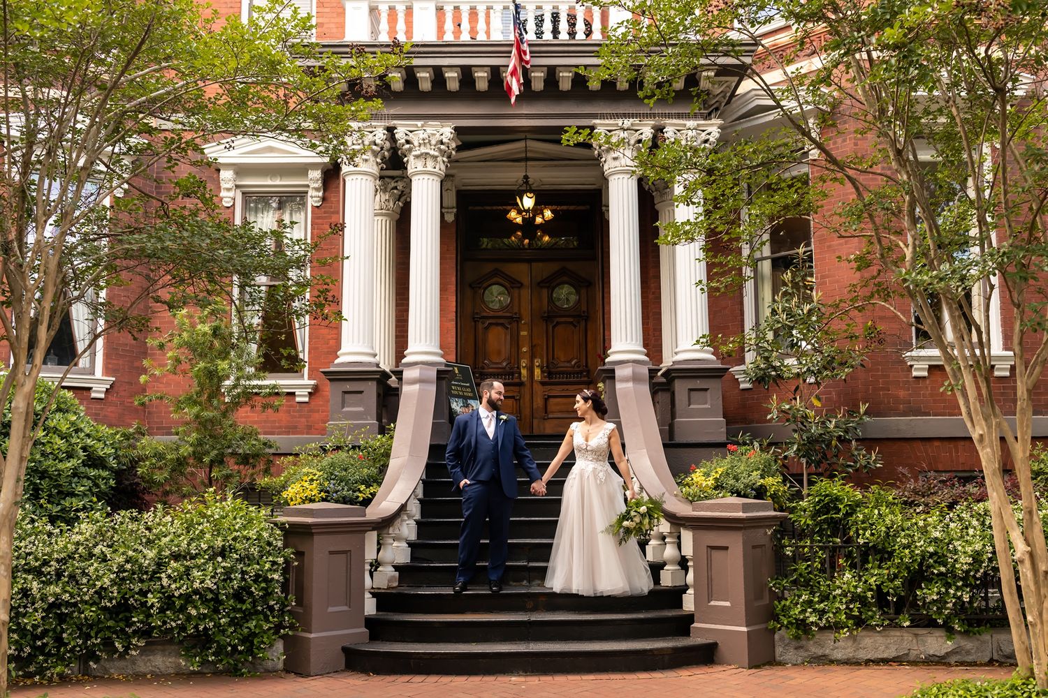 Elegant historic red brick mansion with white trim and Greek Revival columns features a curved front staircase and landscaping.