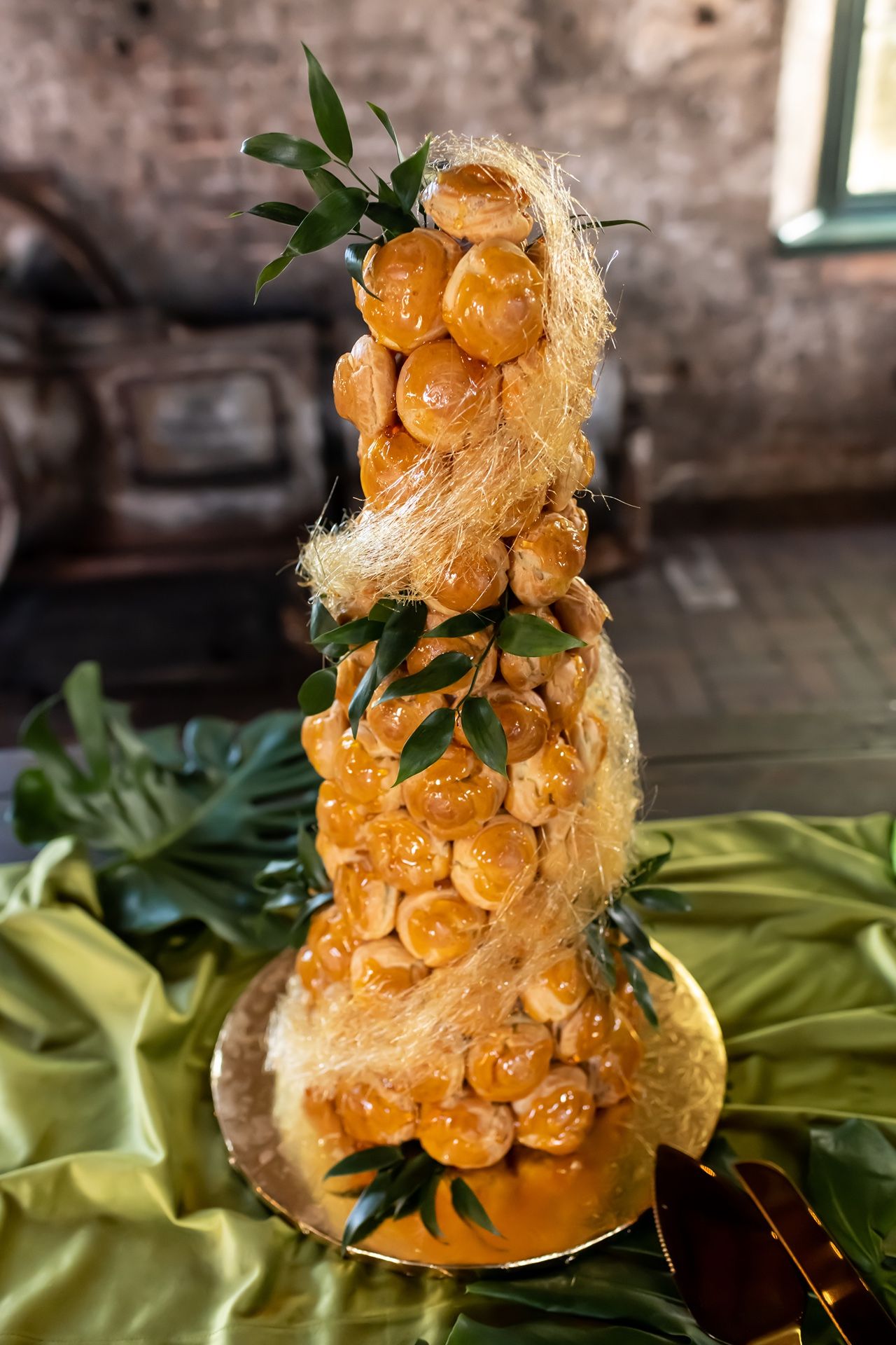 A towering dessert sculpture made of spun golden sugar threads and amber-colored spherical candies atop a green tablecloth.