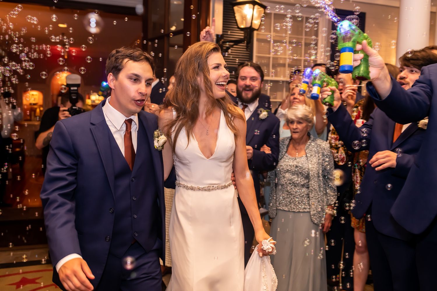 Newlyweds exit their wedding celebration through a shower of bubbles as guests cheer and celebrate.