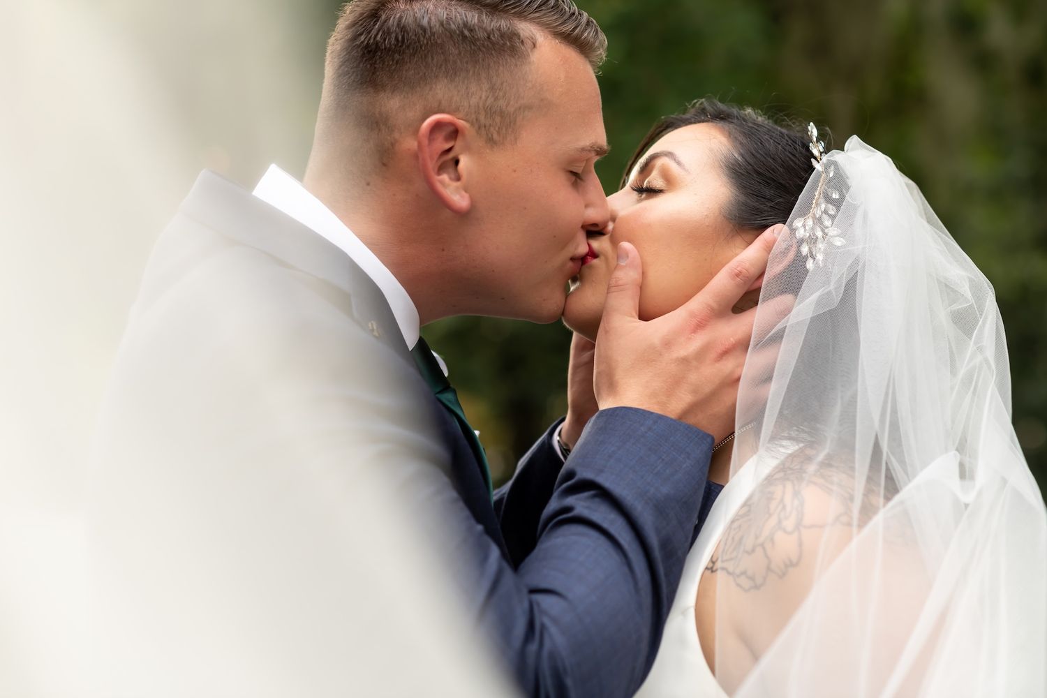A bride and groom share a romantic first kiss at their wedding ceremony, with the veil softly framing the moment.