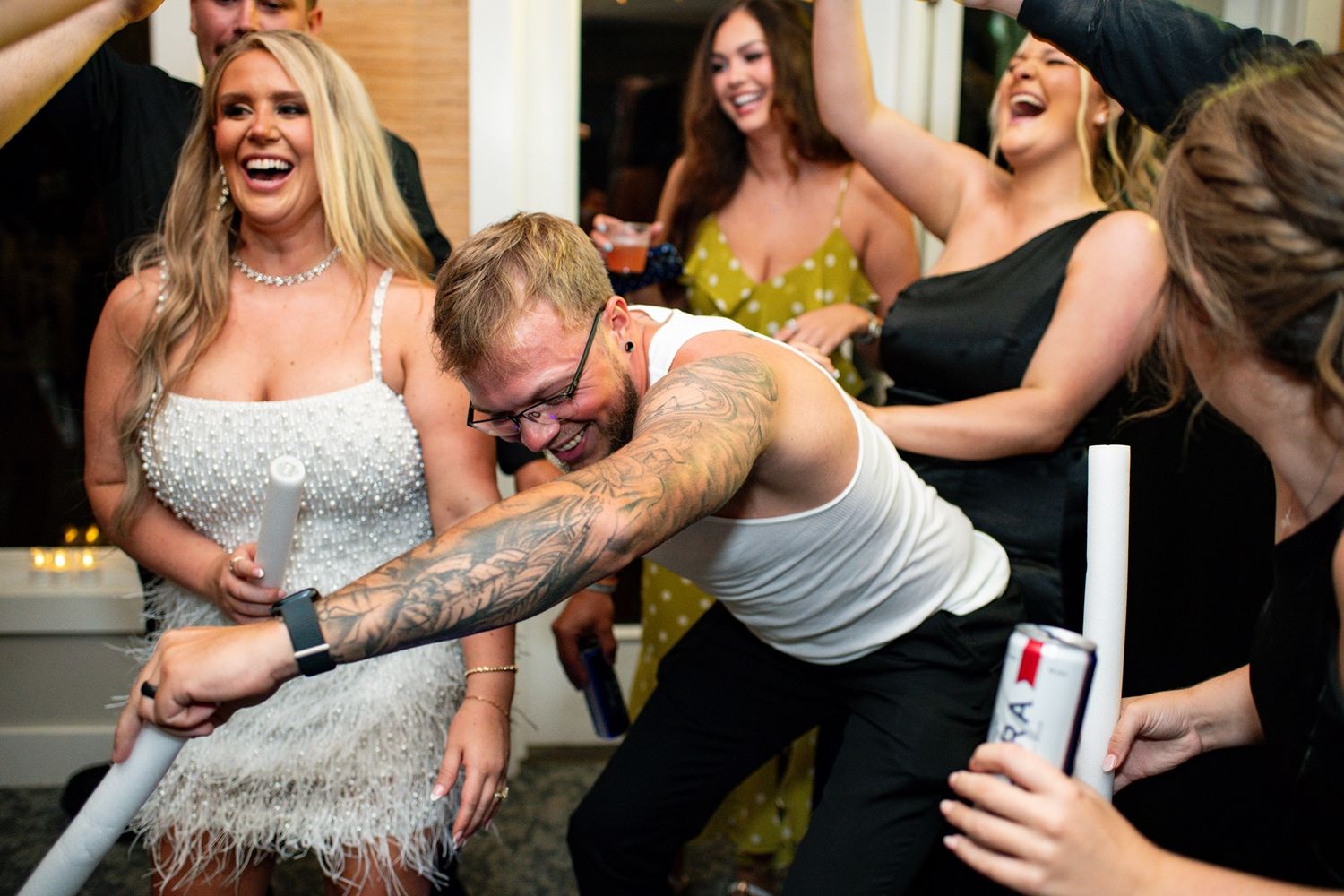 A group of people laugh and dance together at a celebration party with one person wearing a sparkly dress.