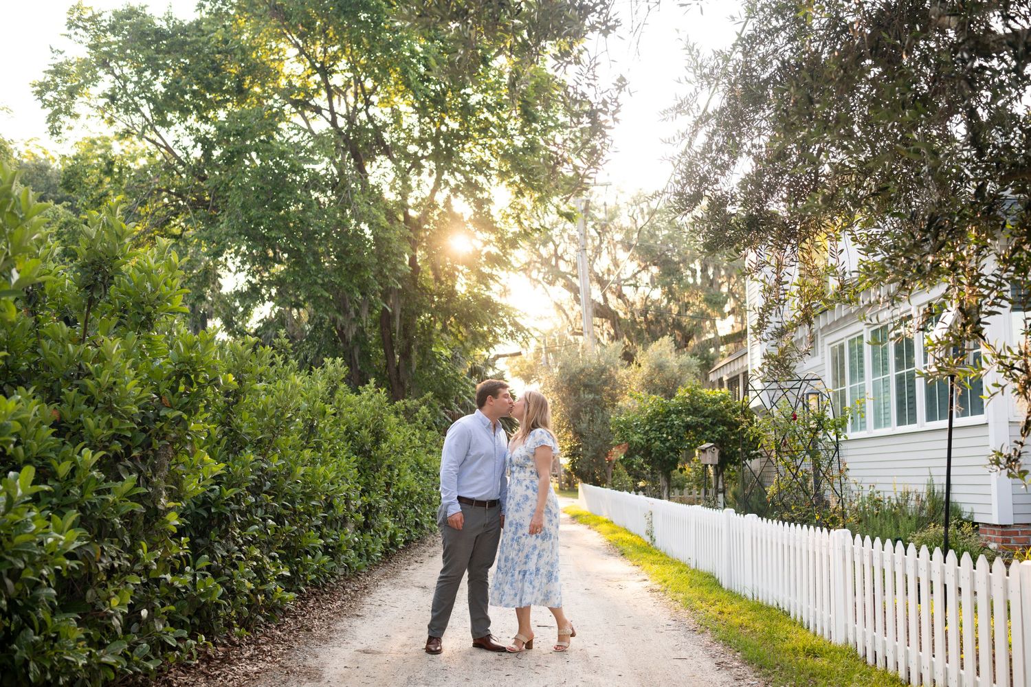 A romantic couple kisses in a pathway with white picket fences during golden hour in Isle of Hope