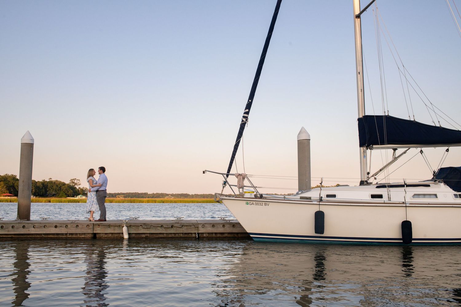 Panoramic view of sailboats and docks at a marina during sunset with calm waters reflecting the golden sky.
