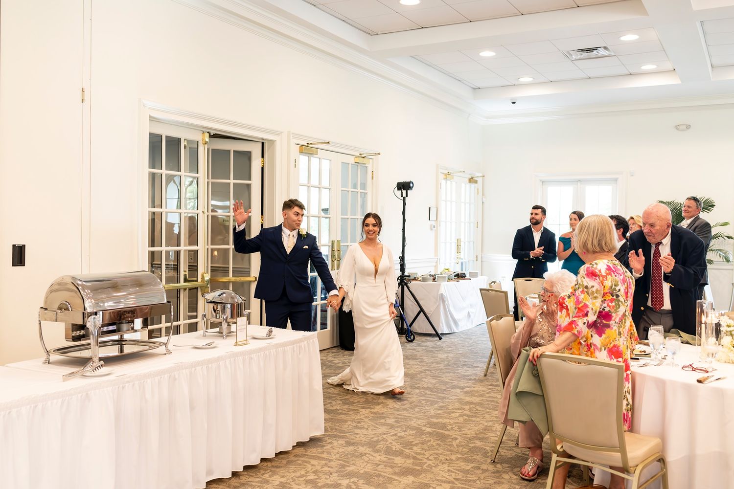 Panoramic view of an elegant white wedding reception venue with floral centerpieces and table settings.