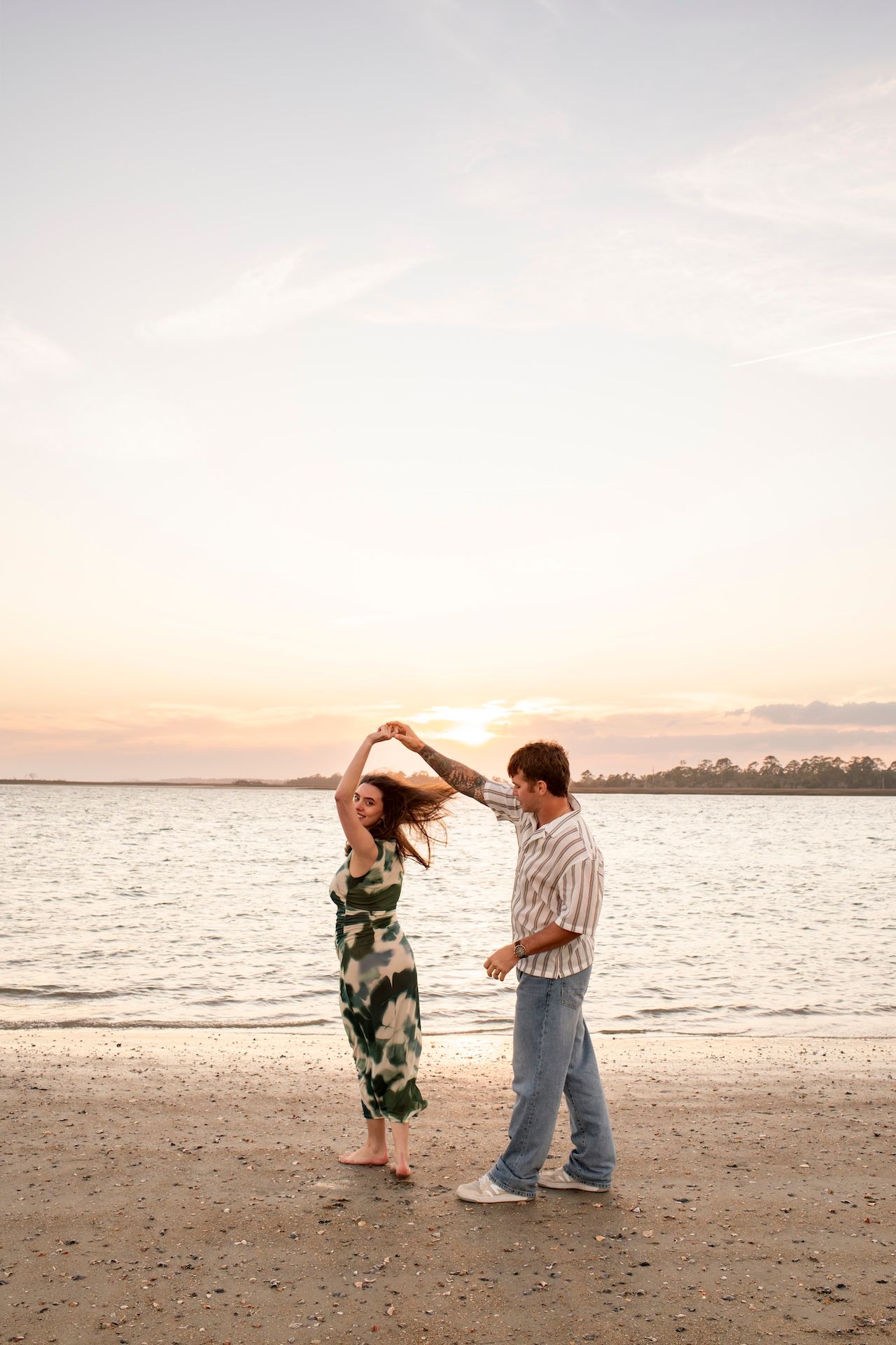 A couple dances together on a beach at sunset, creating a romantic silhouette against the ocean view.