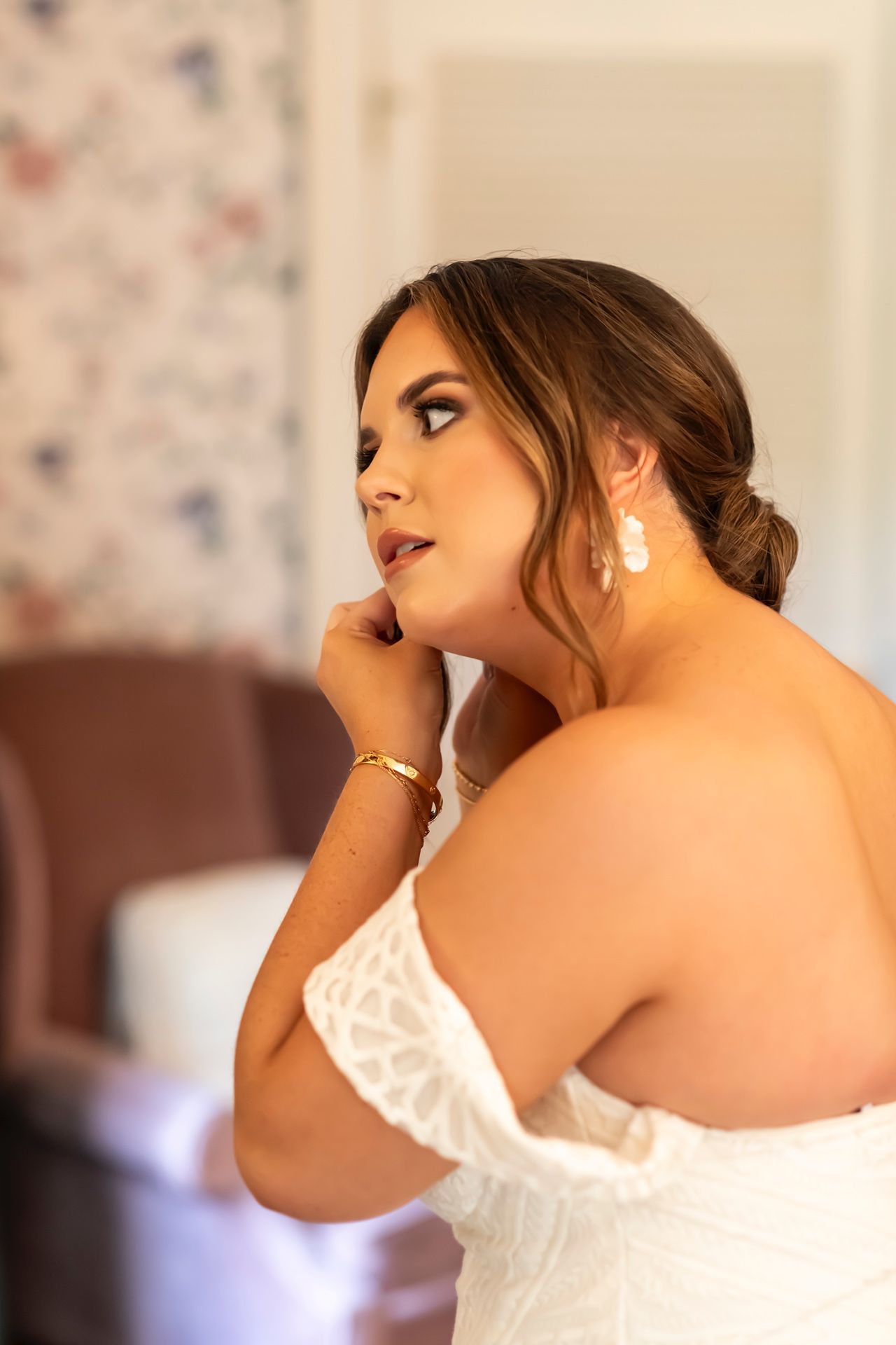 A person wearing a white strapless dress poses elegantly with dangling earrings and an upswept hairstyle.