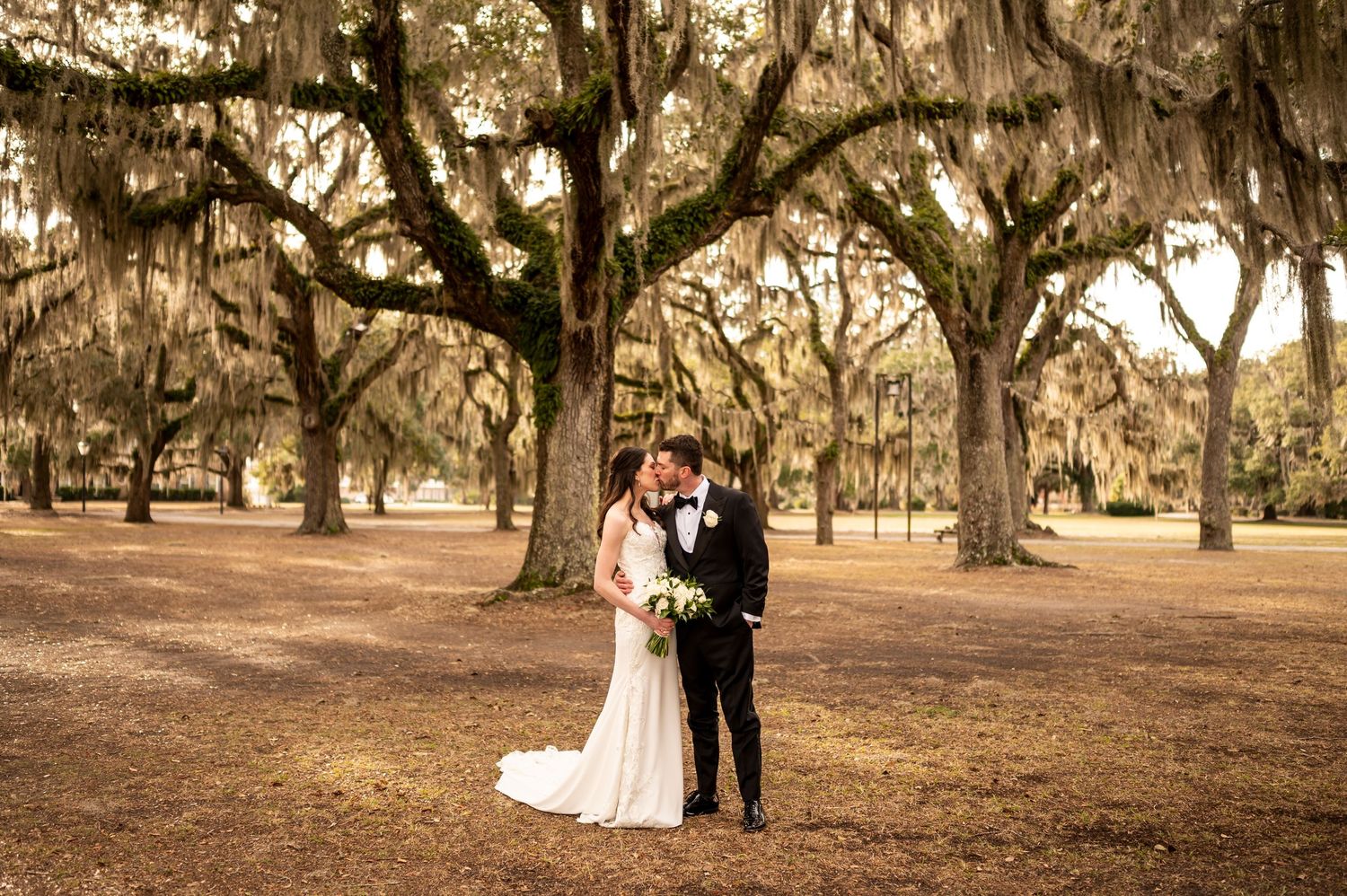 A couple stands beneath stunning Spanish moss-draped oak trees in a romantic outdoor setting during autumn.