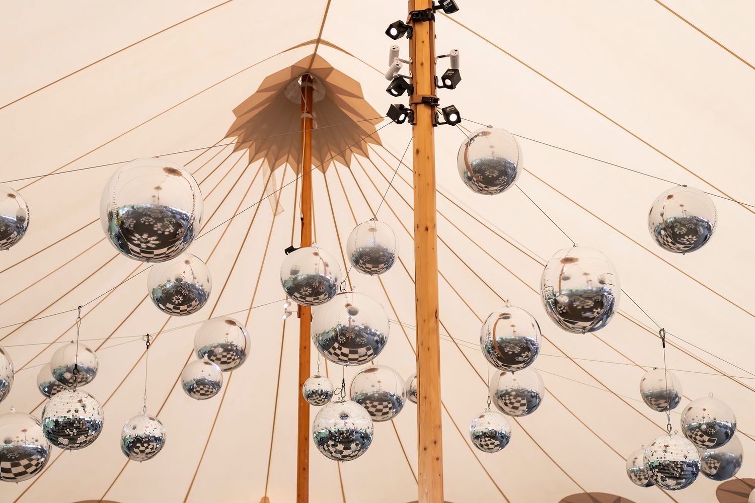 Multiple disco balls hang from the peaked ceiling of an elegant white tent creating a sparkling dance floor atmosphere.