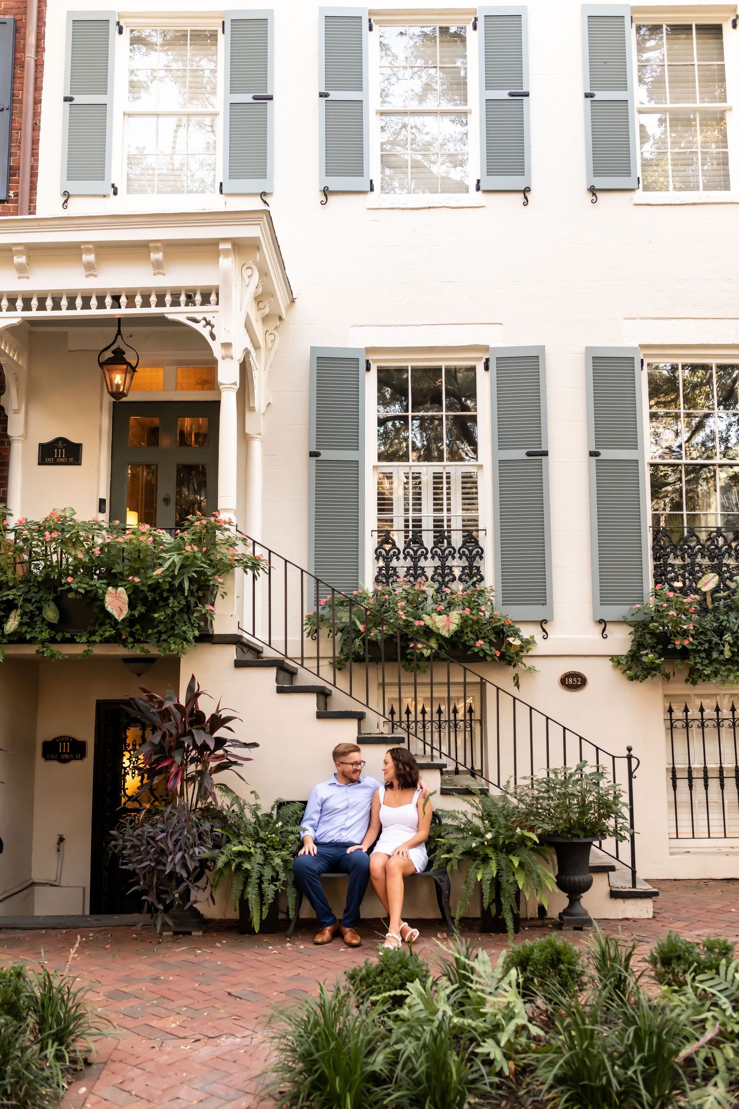 Historic Charleston townhouse with light gray shutters, brick steps, and lush greenery adorning the entrance.