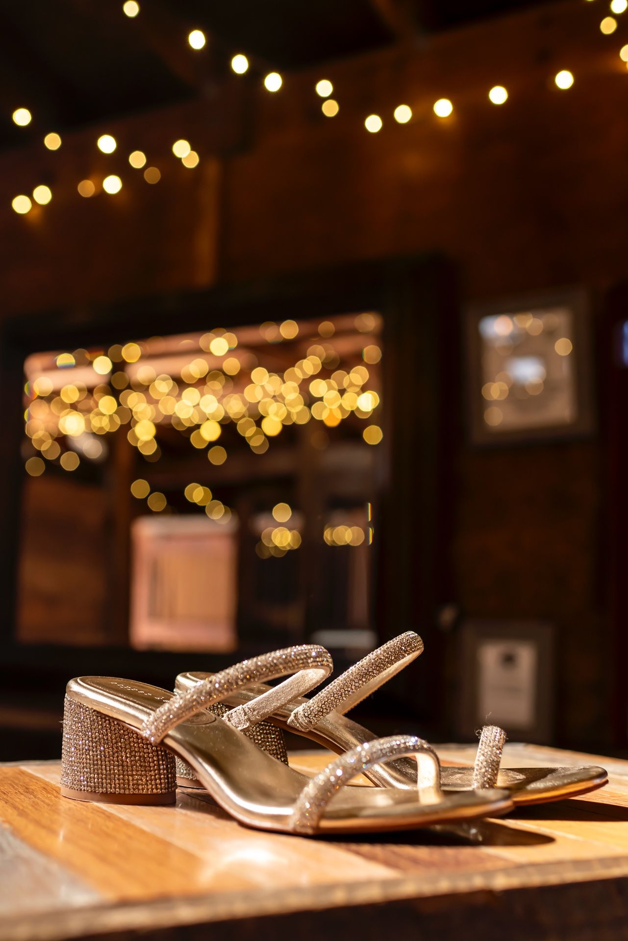 Sparkly silver sandals arranged in a row on a wooden table with twinkle lights in the background.