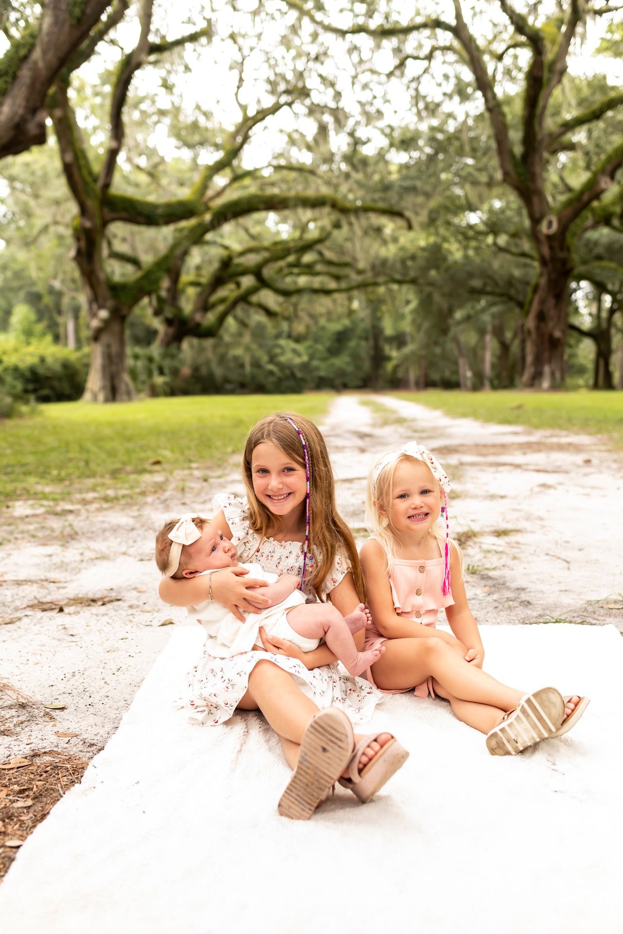 Children and puppy sit together on a sandy path under majestic oak trees draped with Spanish moss.