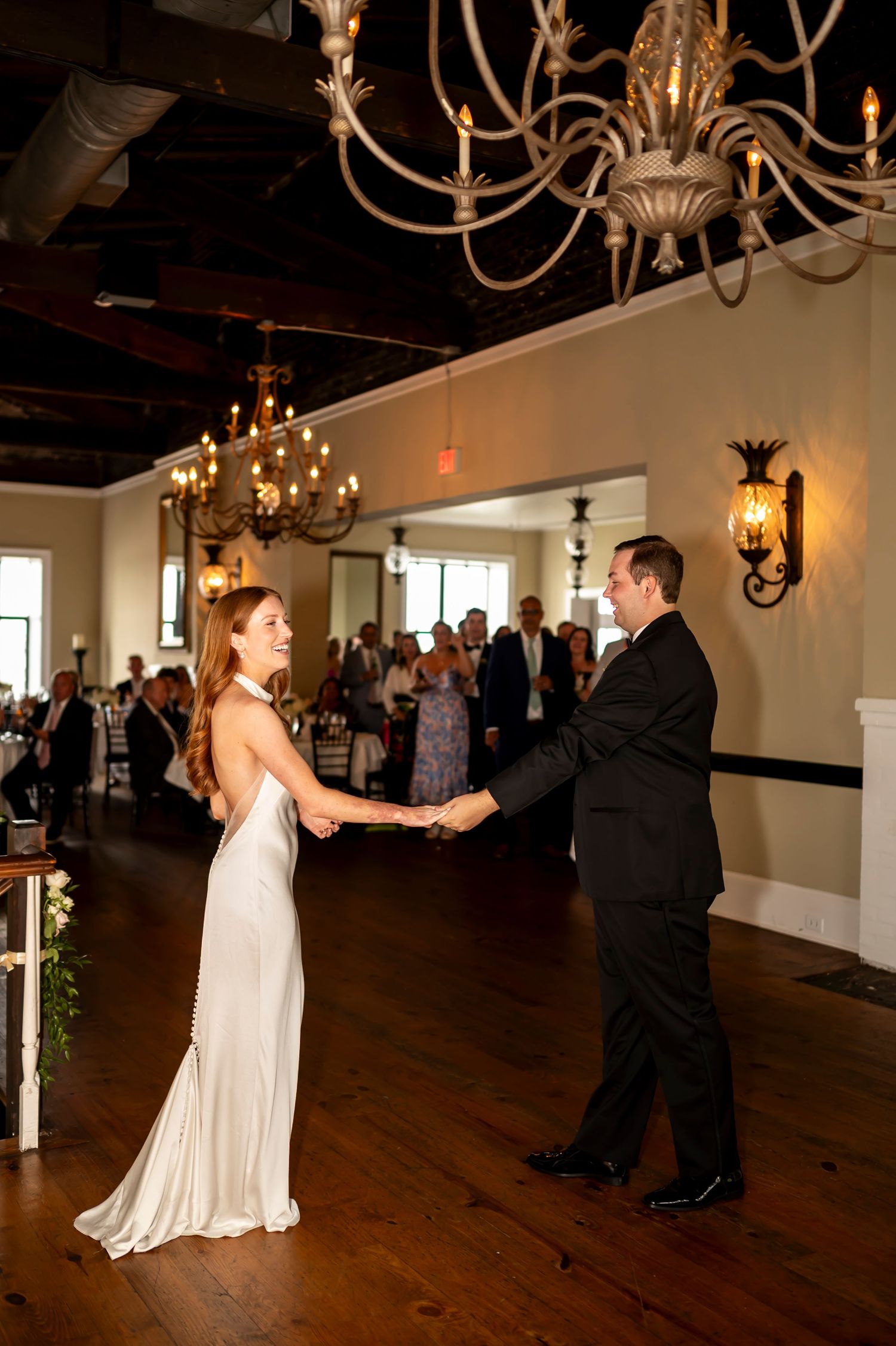 Dancing figures move gracefully across a polished hardwood floor under elegant chandeliers at an indoor ballroom venue.