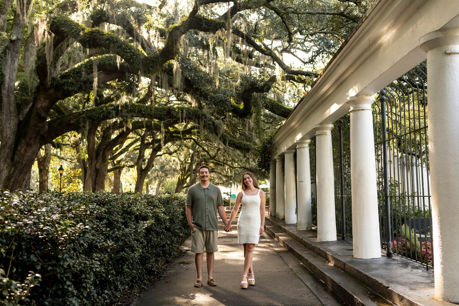 A covered walkway with white columns and hanging Spanish moss creates a serene garden path at Airlie Gardens.