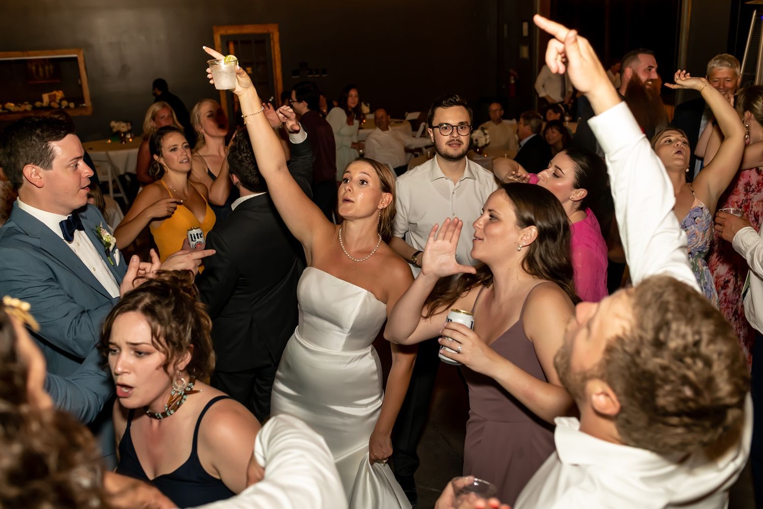 A crowded dance floor of people enthusiastically dancing and raising their arms at a party or celebration.