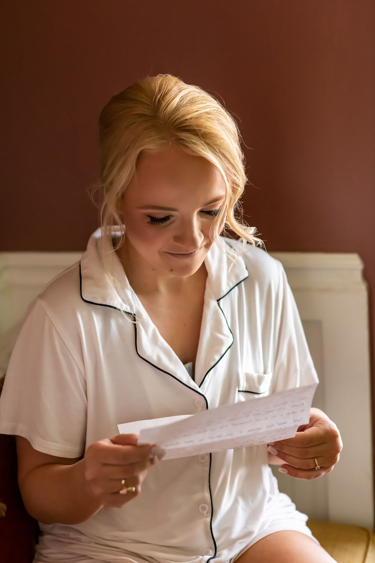 Person in white silk pajamas reads letter while sitting on couch during morning preparations.