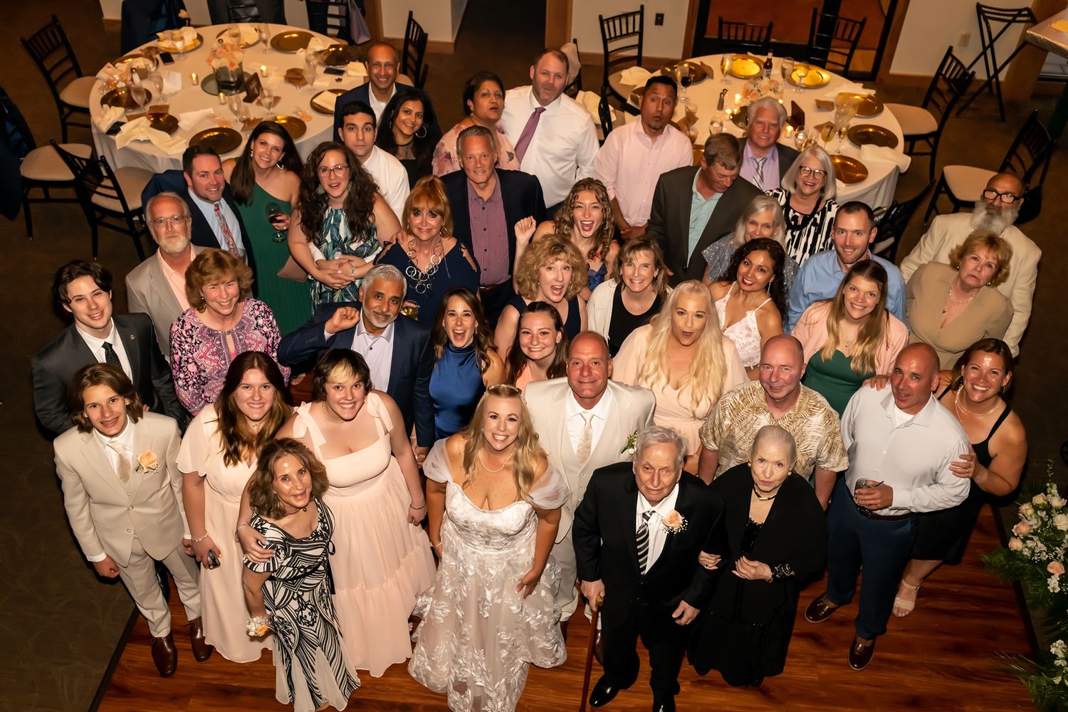 Large group of wedding guests gathered together posing for an overhead photo in an elegant reception venue.