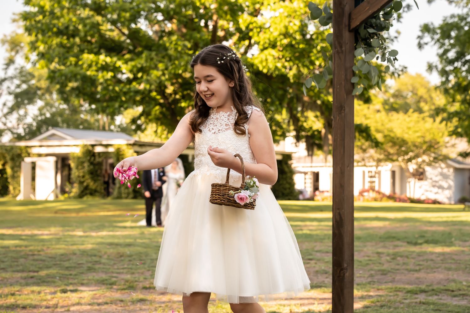 Someone in a white tulle dress stands outdoors in a sunny park setting while holding a small purse.