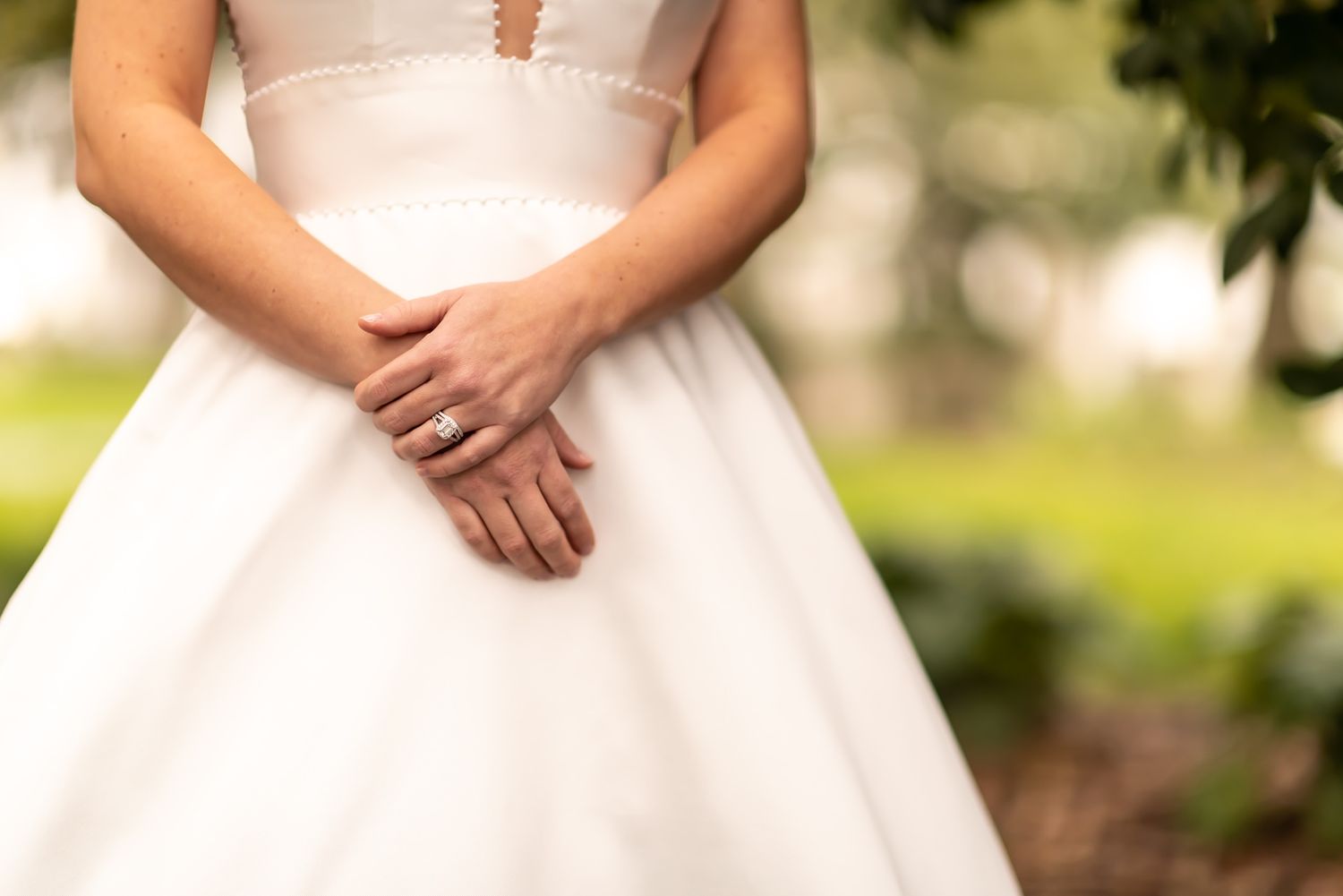 A person in a romantic white lace wedding dress poses in a sun-dappled garden setting.