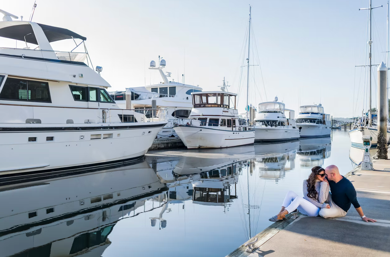 Several luxury yachts and boats docked at a marina with calm waters reflecting the vessels on a sunny day.