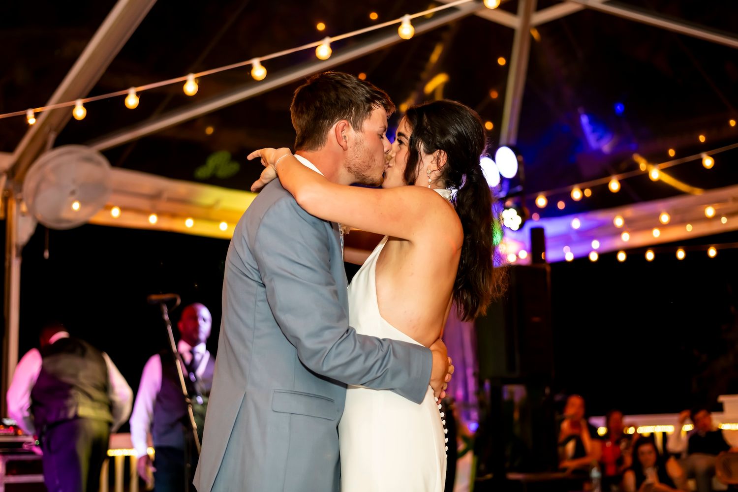 A couple dances together under twinkling string lights at an evening outdoor wedding reception.