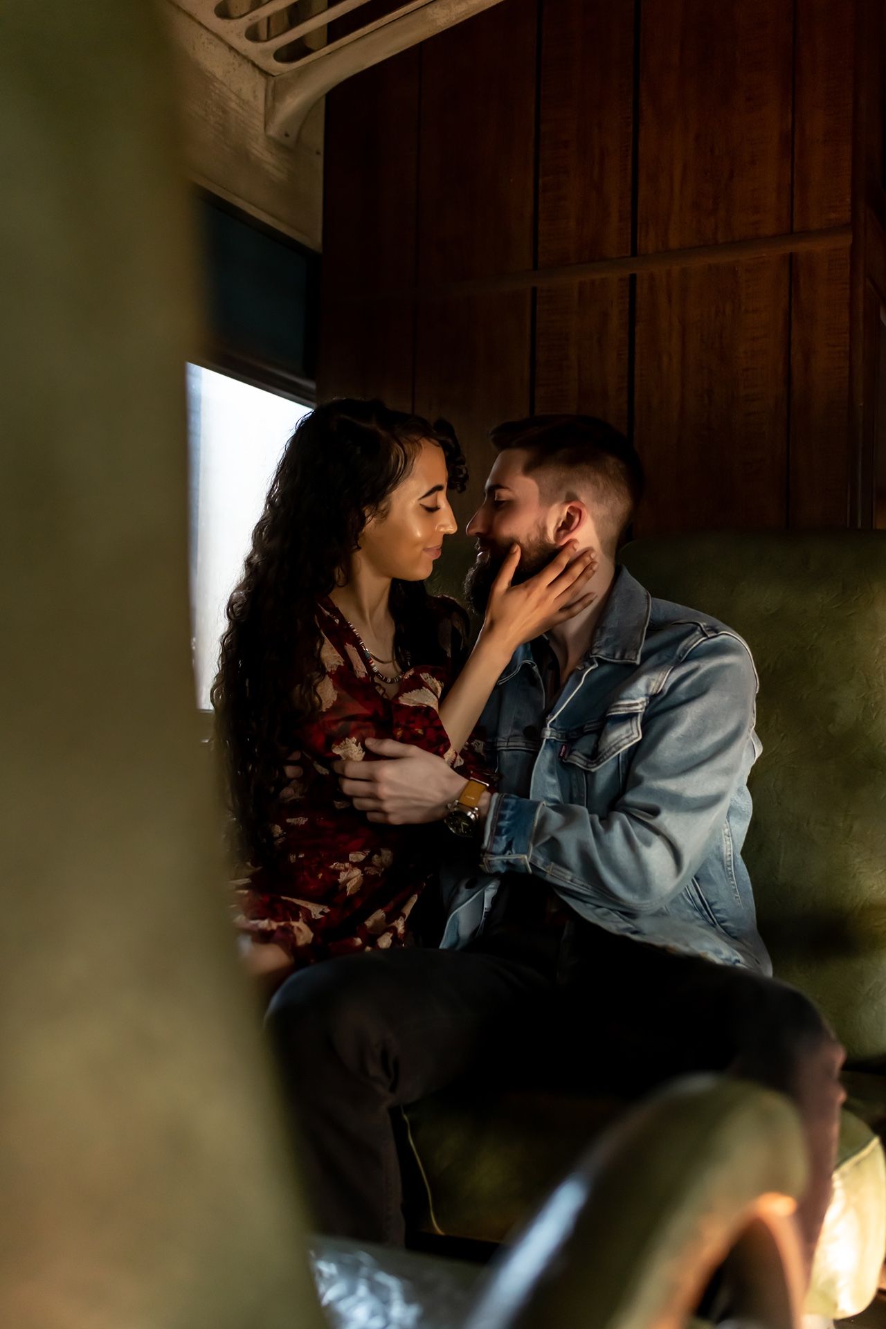 A romantic couple sharing an intimate moment in moody lighting against wooden paneling.