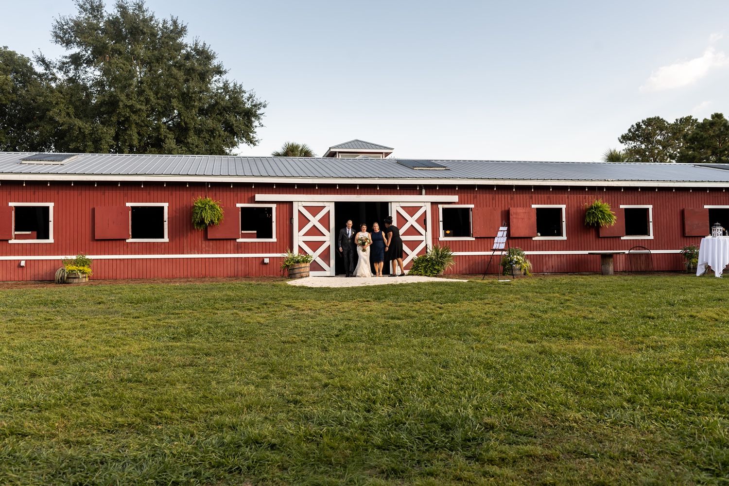 Long red barn with white trim and multiple Dutch doors sits on a grassy field on a sunny day.