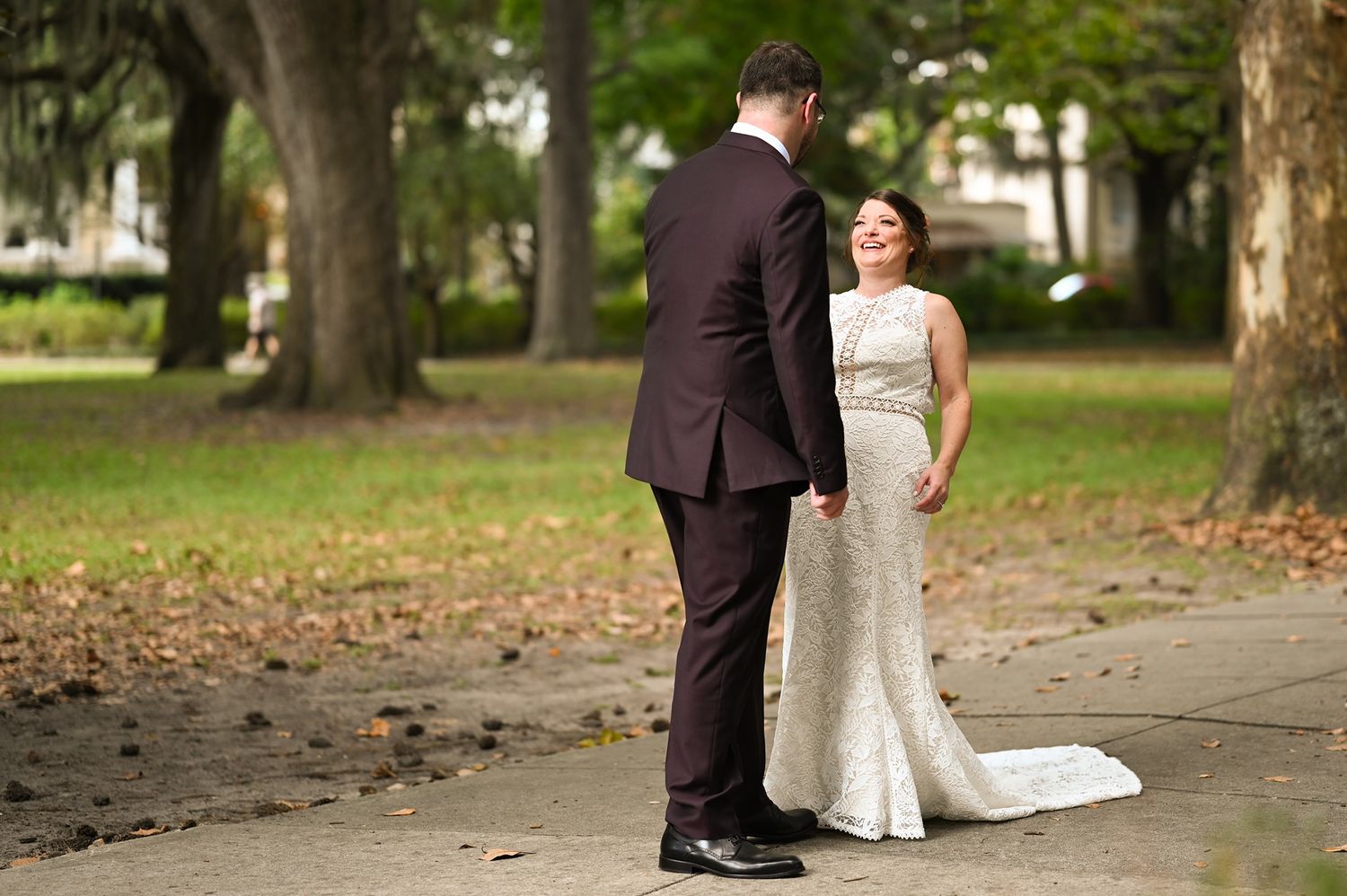 Bride and groom walking on a tree-lined path in a park during their wedding photo session.