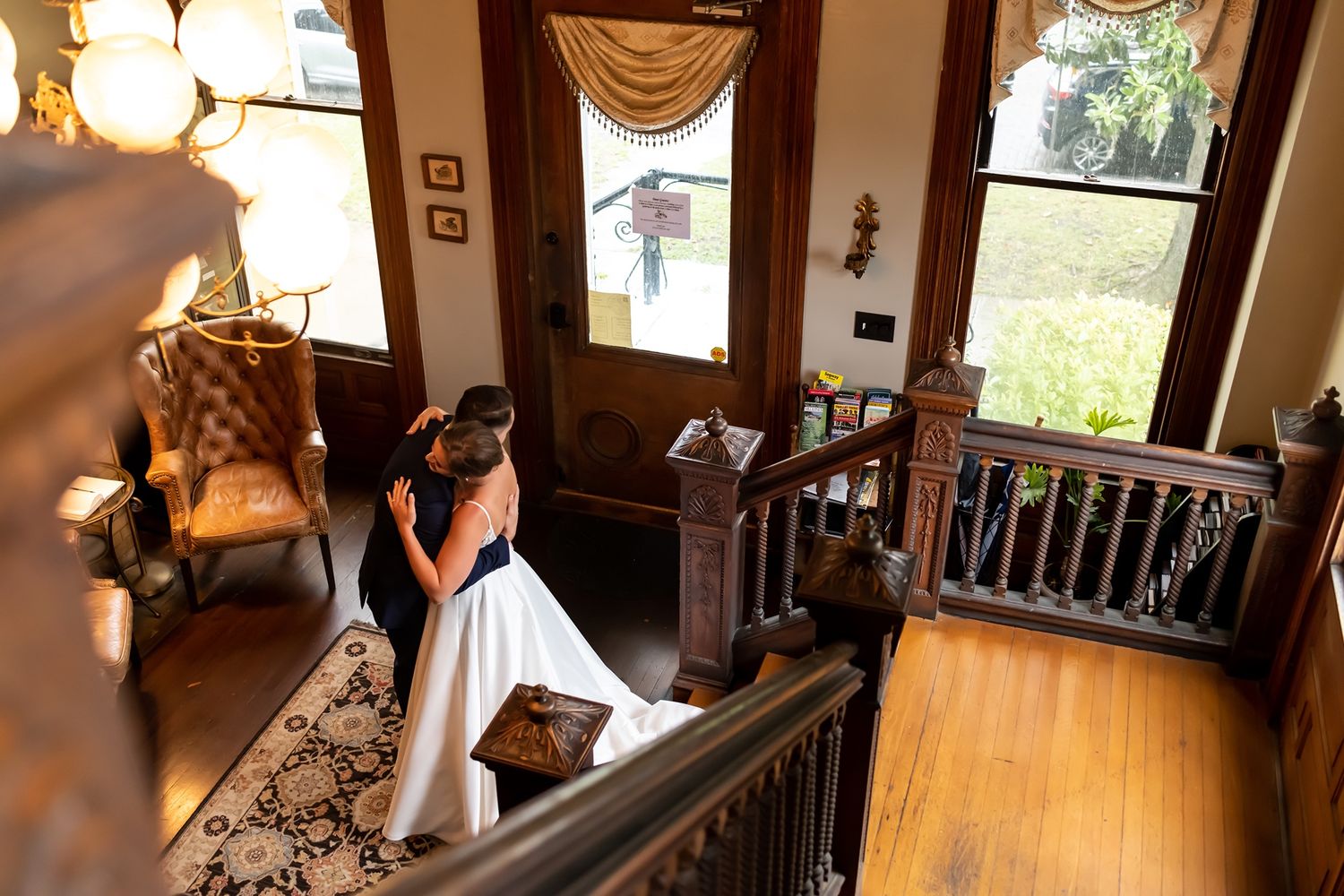 A couple stands together on an elegant wooden staircase in a historic home interior.