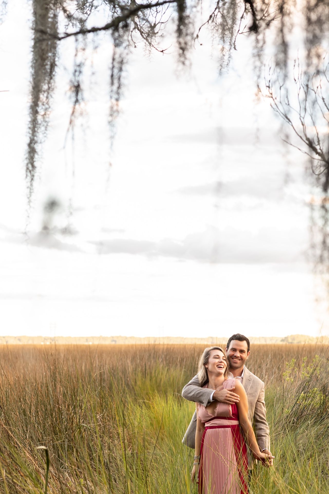Couple capturing intimate moments together in a golden grass field under spanish moss trees.