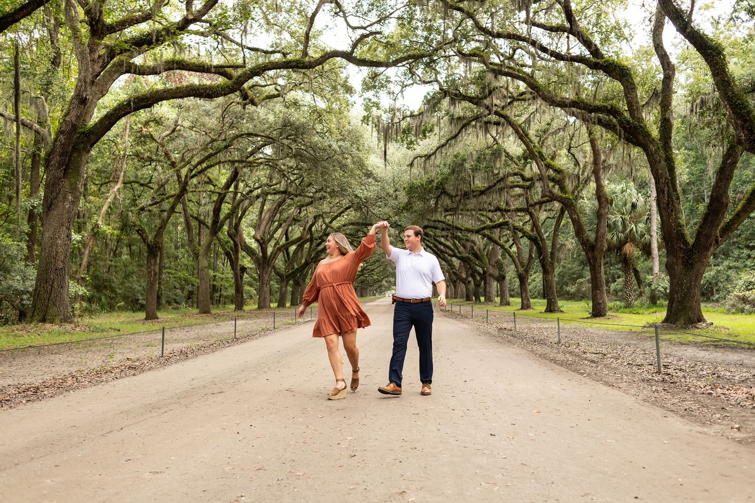 A romantic moment unfolds along a winding trail beneath majestic oak trees covered in hanging moss.