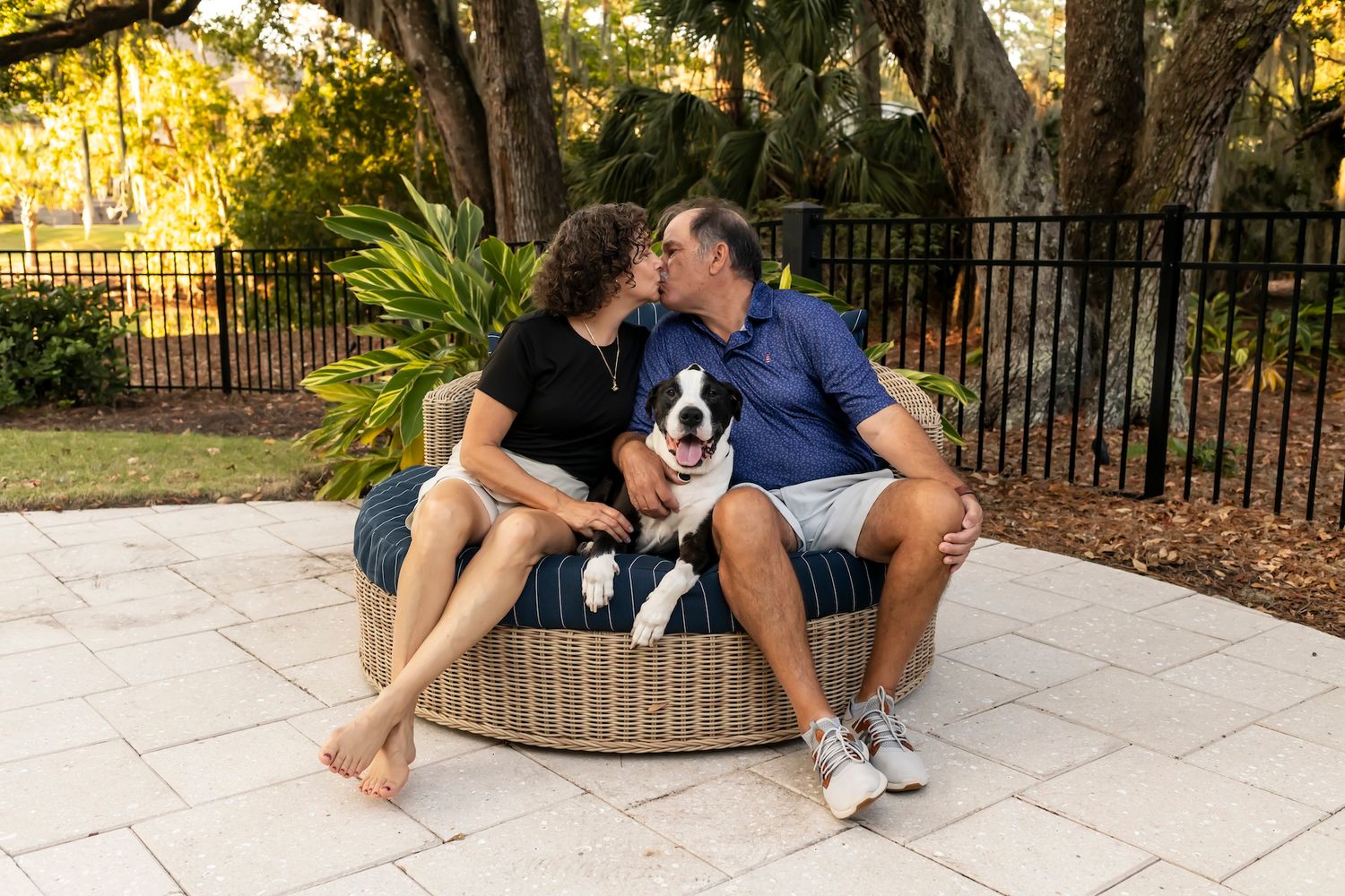 A couple sits on outdoor furniture with their black and white Border Collie dog on a patio.