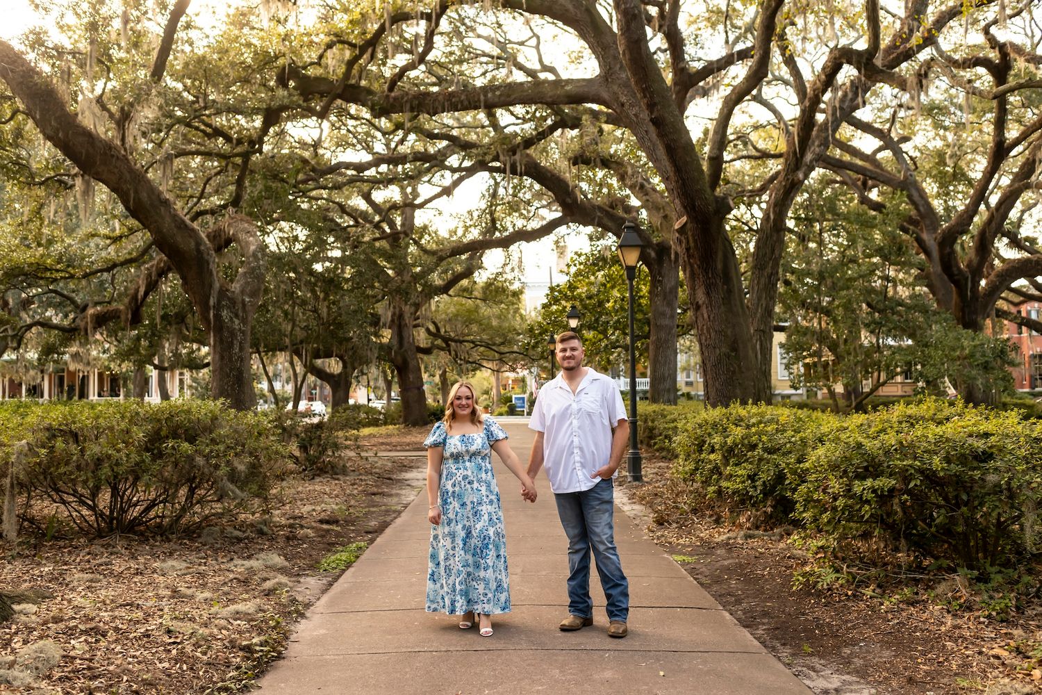 A couple walking hand in hand down a tree-lined pathway in a park.