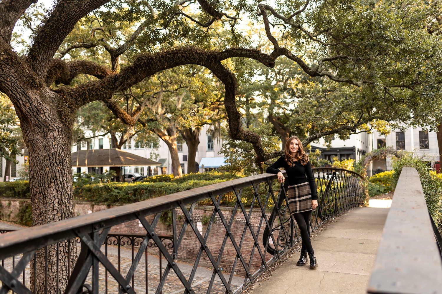A pathway with iron railings lined by moss-draped oak trees in a scenic urban park setting.