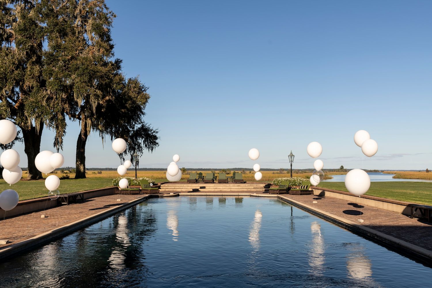 White decorative spheres line a reflecting pool surrounded by palm trees at an elegant outdoor venue by the waterfront.