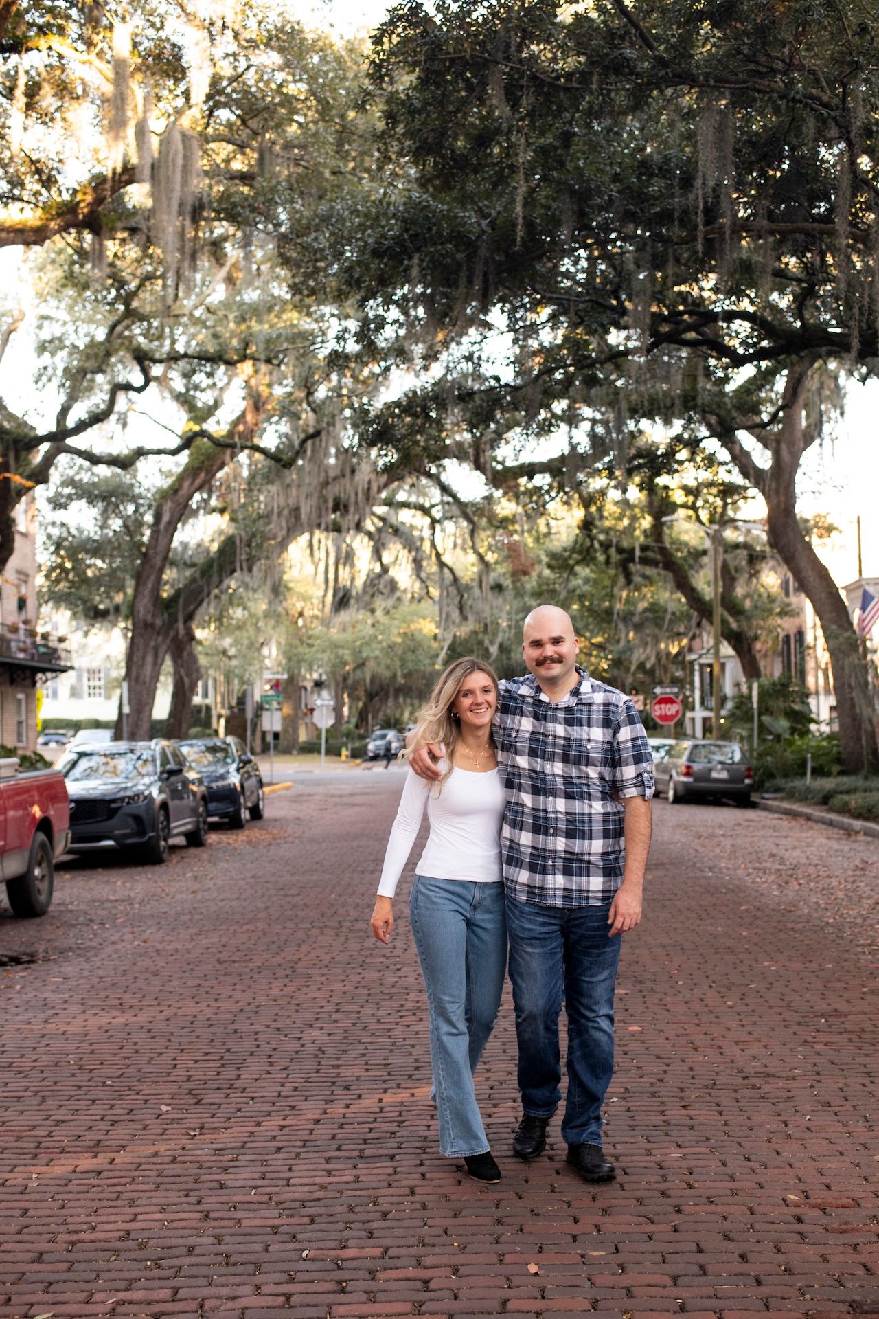 A couple walking together on a brick paved street lined with Spanish moss-draped oak trees in Savannah.