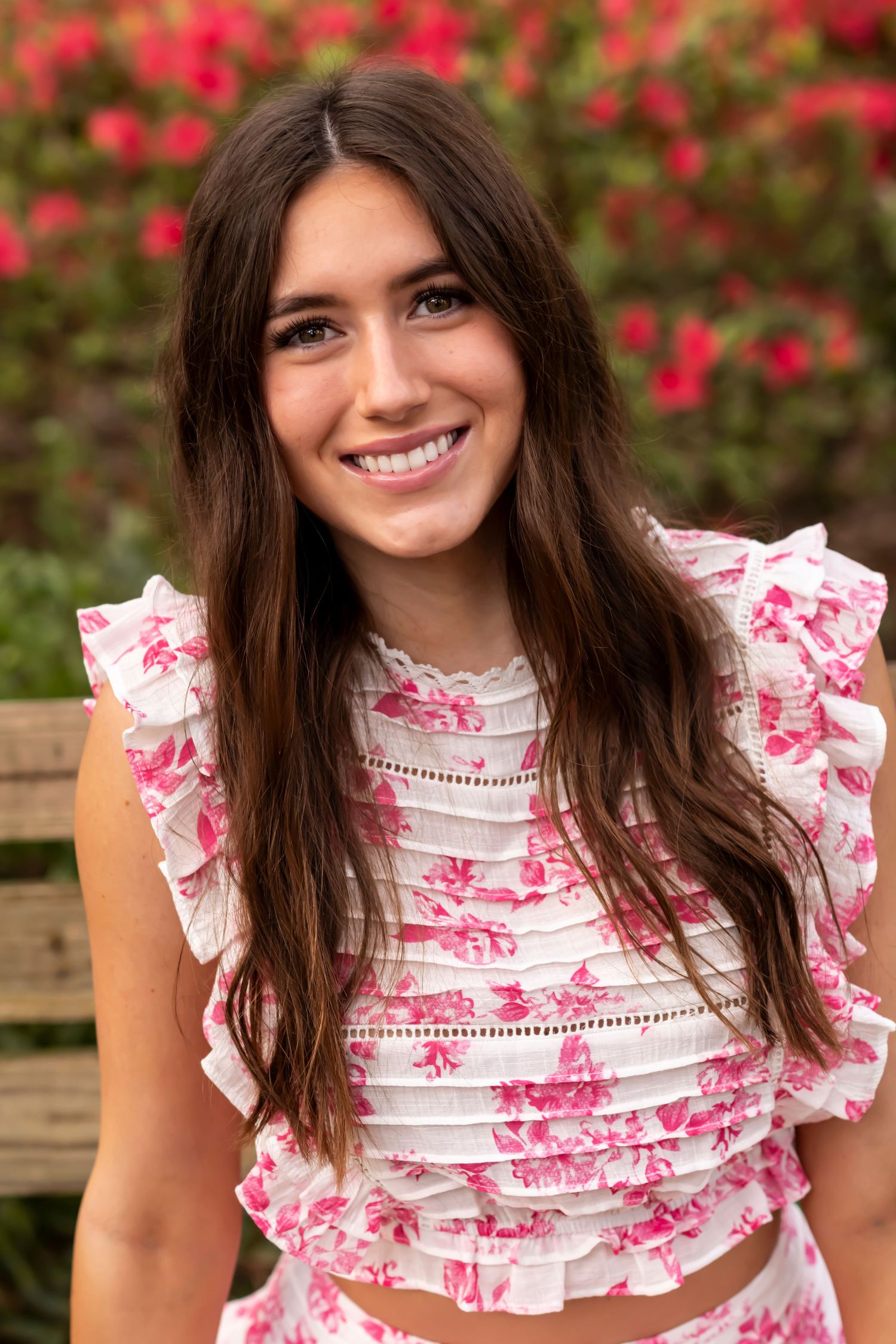 Portrait against pink flowers wearing white and pink floral ruffled crop top.