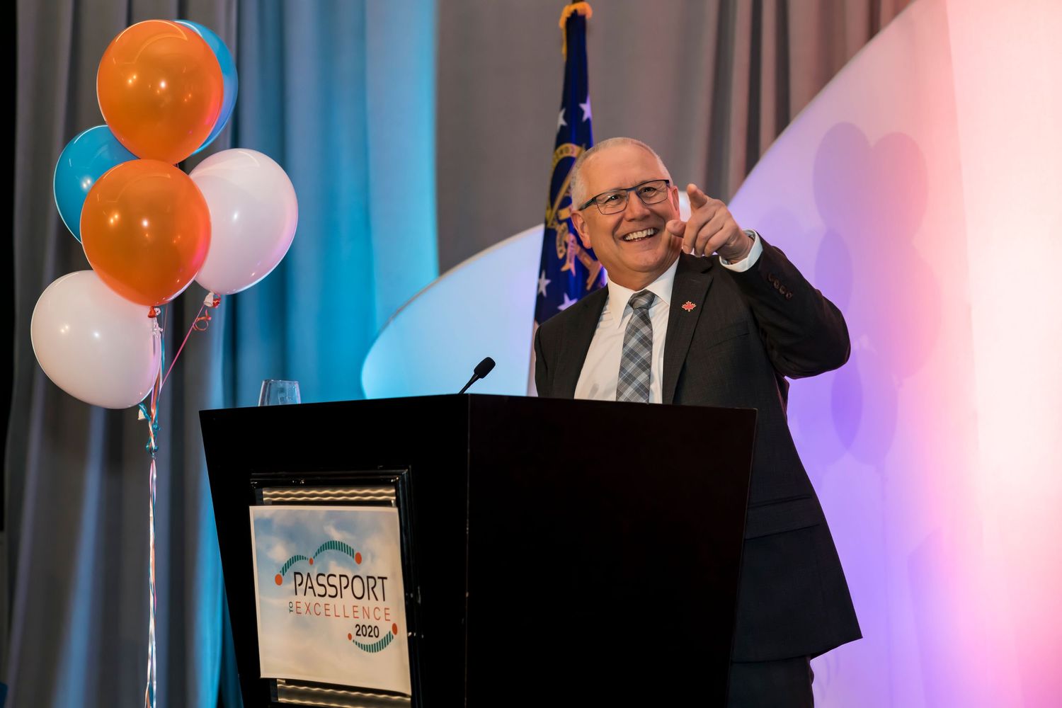 Speaker at podium with orange and white balloons giving enthusiastic presentation at professional event.