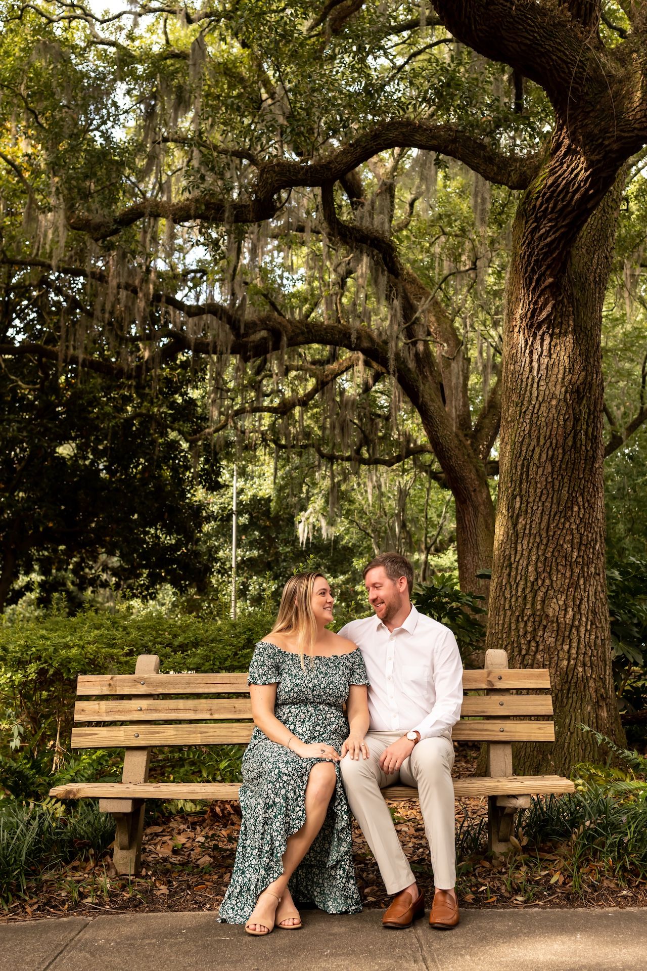 A couple sits together on a wooden bench under a majestic Spanish moss-draped oak tree in Forsyth Park.