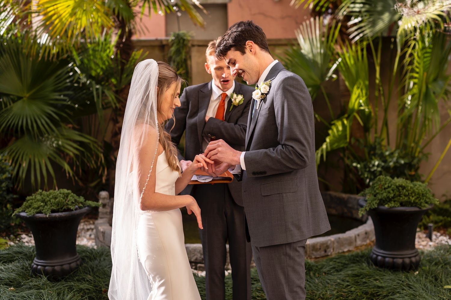 Two people share an intimate moment during their outdoor wedding ceremony surrounded by tropical palm plants and greenery.