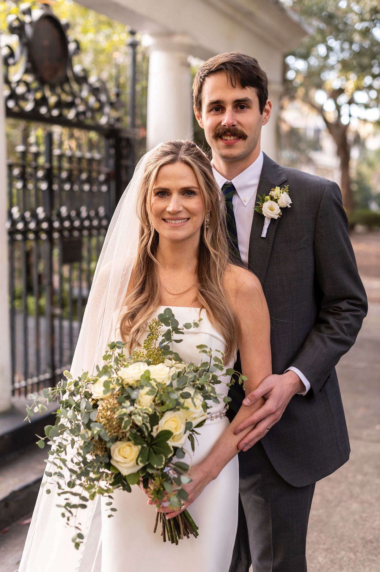 Elegant outdoor wedding portraits featuring a couple in formal attire with white and yellow bouquet among garden gates.